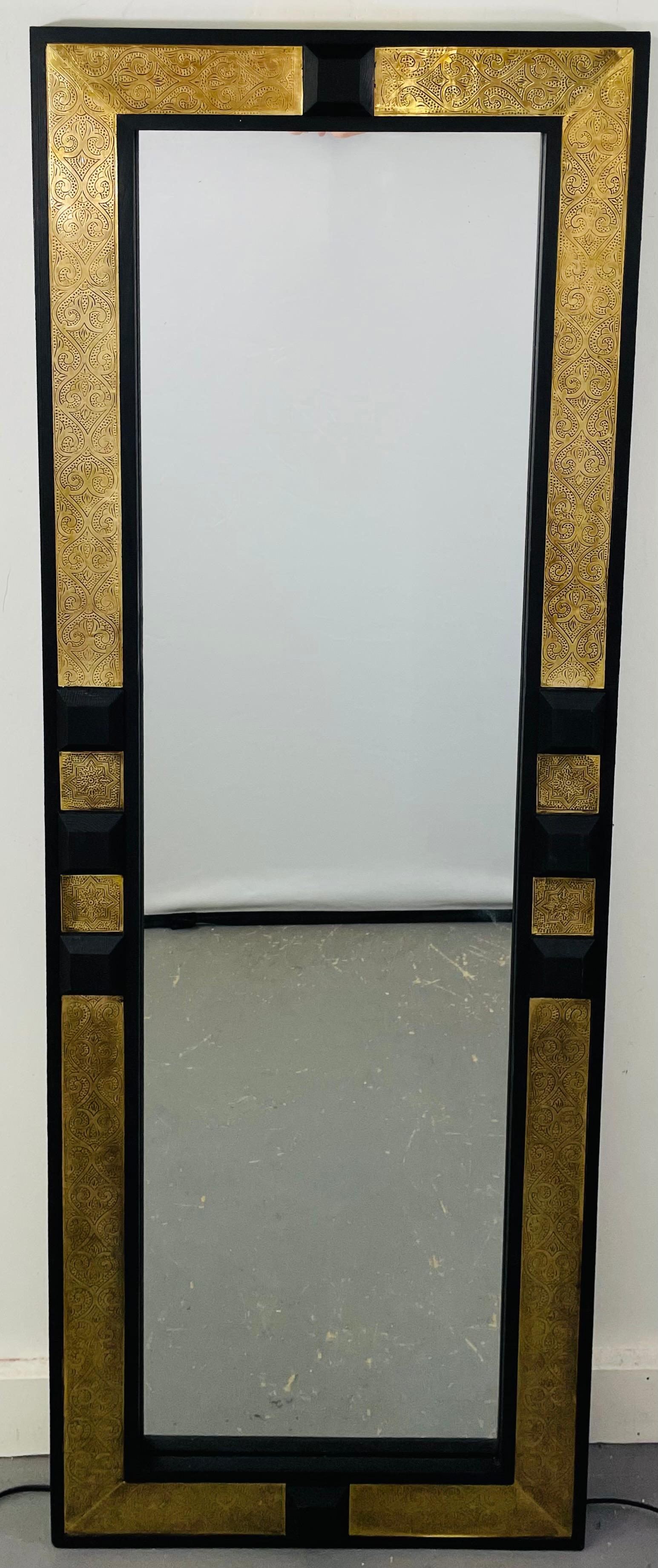 An elegant pair of Hollywood Regency gold brass and ebony wood framed pier or wall mirrors. The frame is handcrafted with gold brass over ebony wood and features beautiful motif design elements, these exquisite mirrors bring a sense of robust