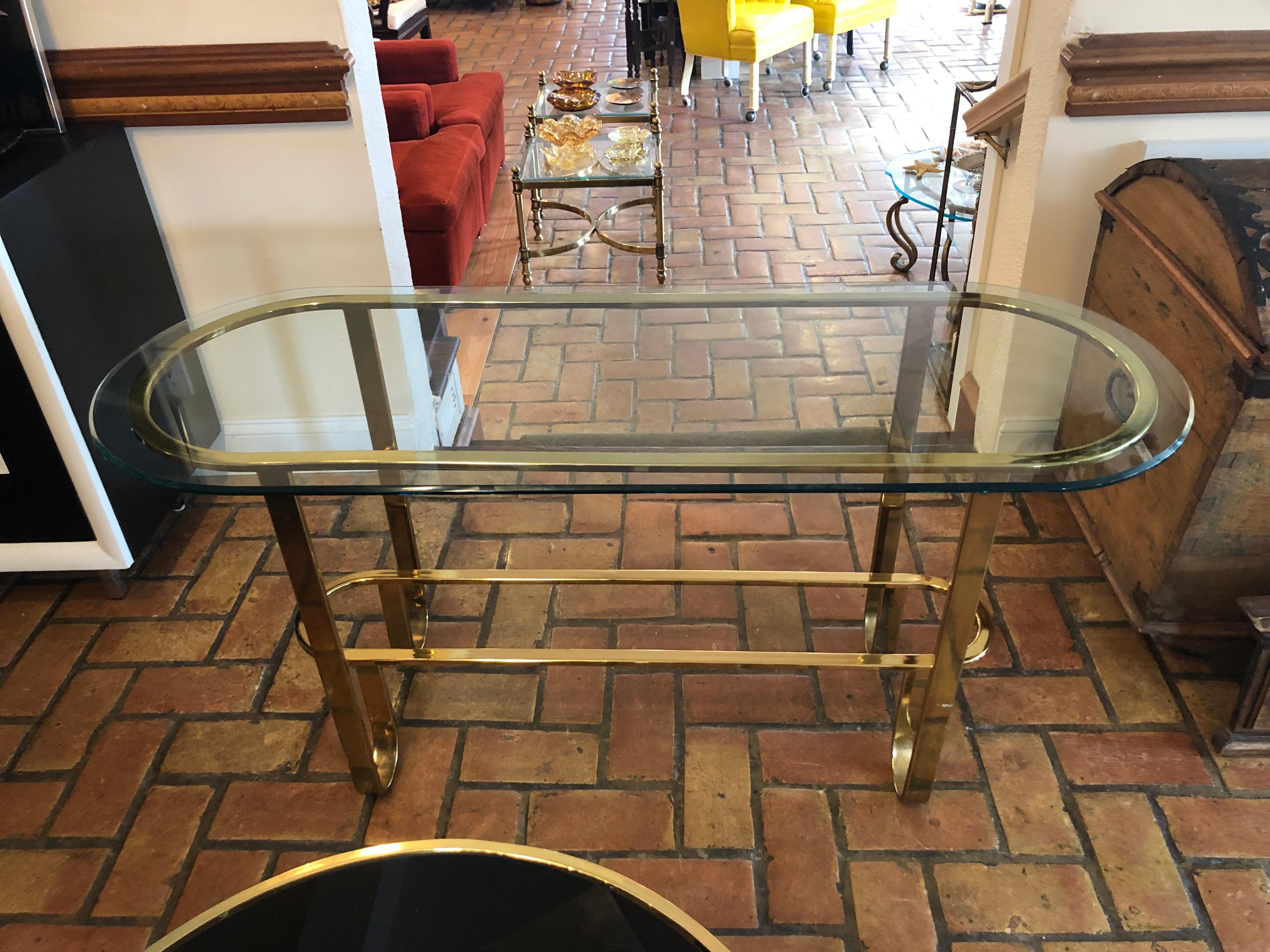Hollywood Regency brass and glass console table. Nice, Minimalist racetrack design. Glass top is loose so not recommended for homes with children. Polished, electroplated brass. Designed by Milo Baughman for by Design Institute of America.