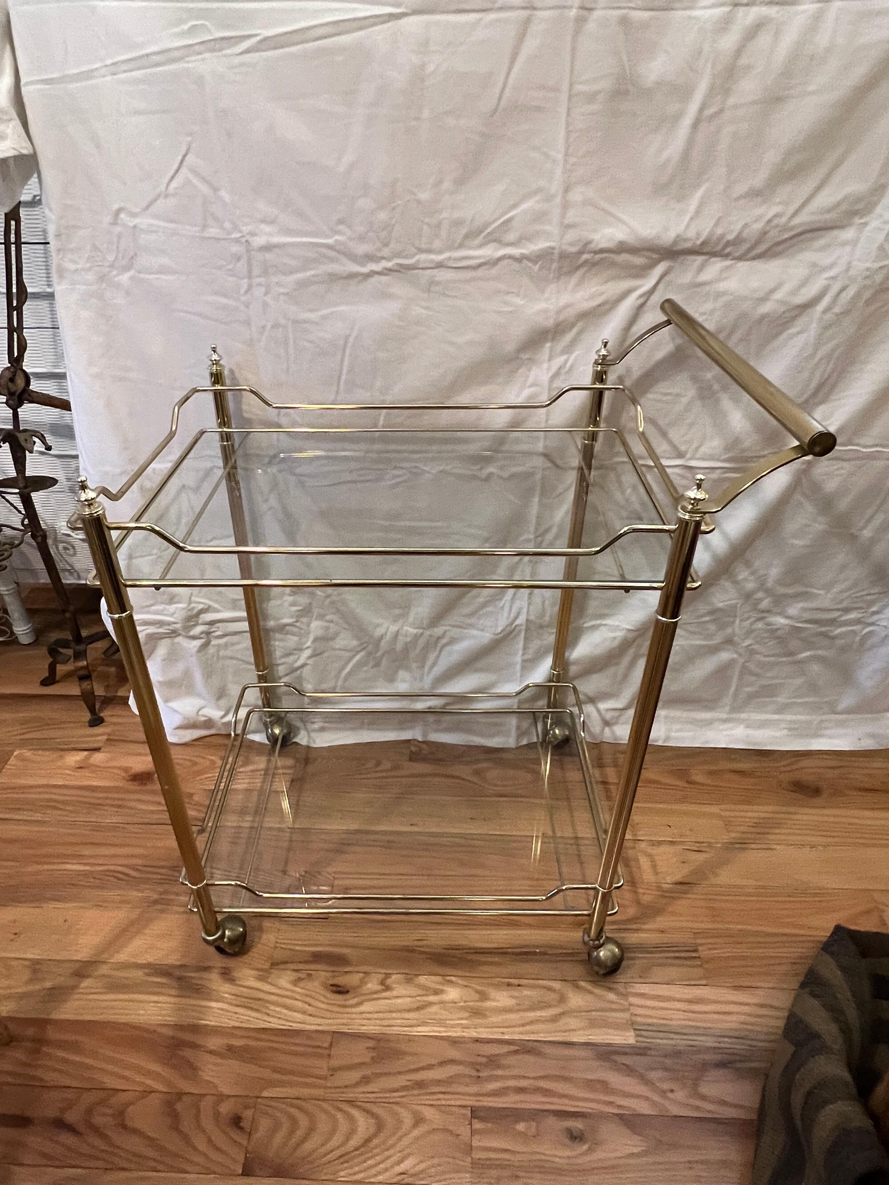 Hollywood Regency two tiered brass and glass bar cart /serving trolley. Nice strong handle to puch around. as well as round rubber castors with a brass lid. Perfect for that small entertaining space.