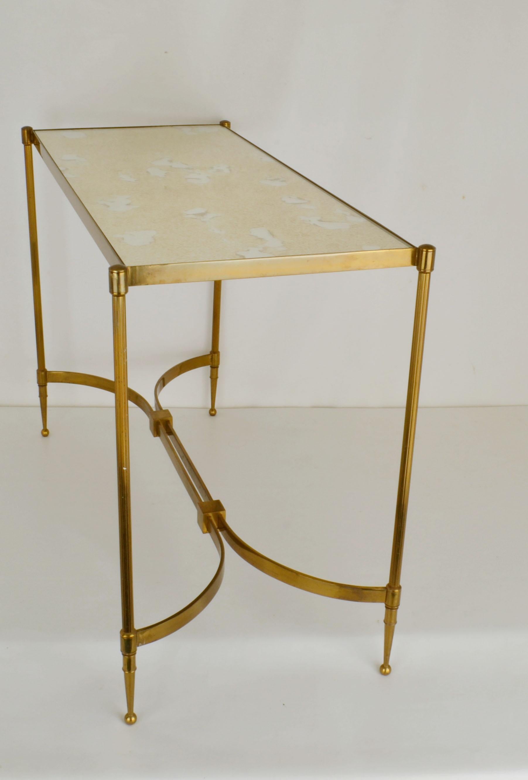 Elegant French rectangular brass coffee table with oxidized mirrored glass that sits on top. The four reeded legs are joined together by two bowed rectangular stretchers joined by two square central finials. The straight shaped table leg as a series