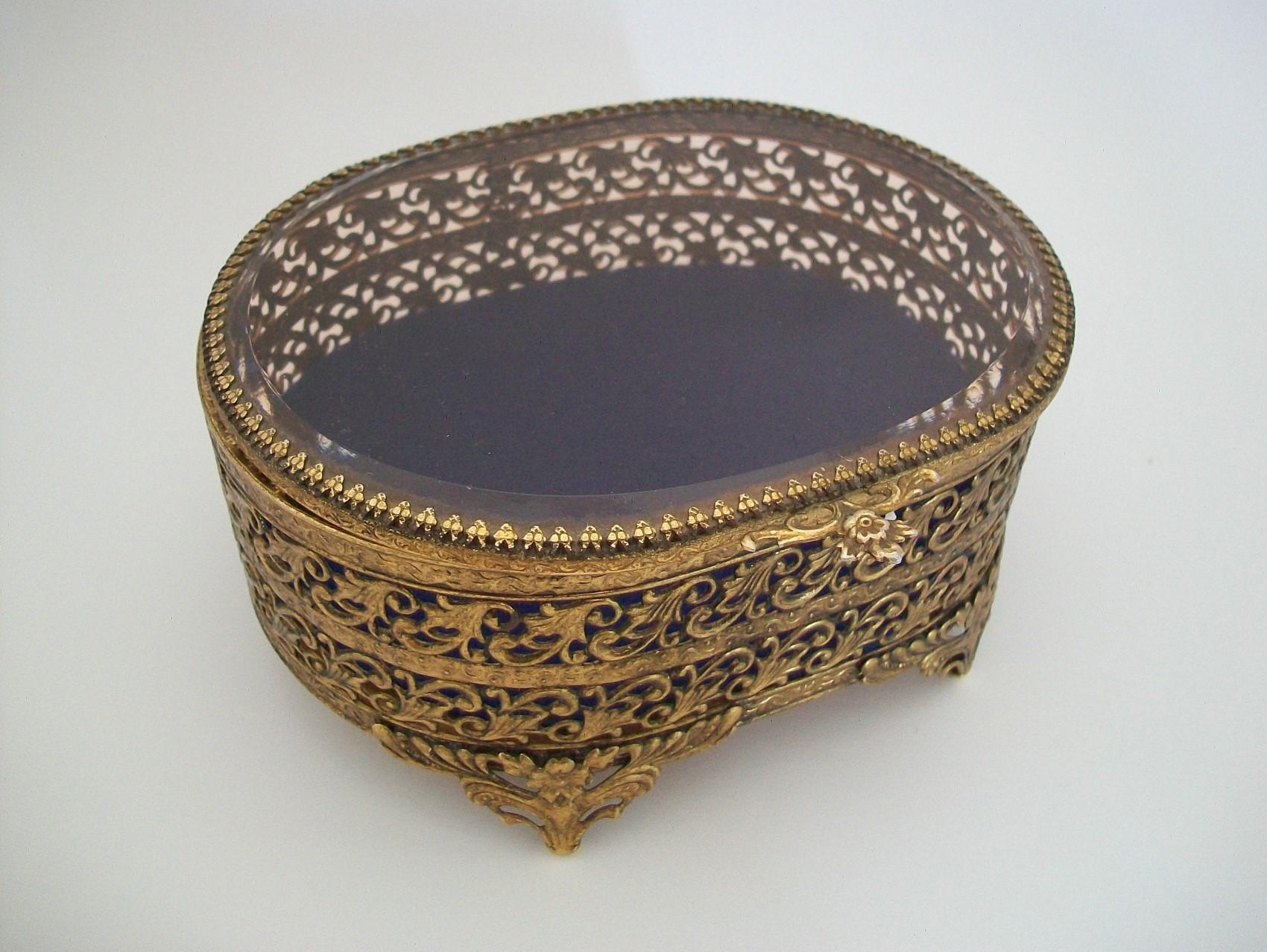 Hollywood Regency brass filigree and smoky topaz glass jewelry box with hinged lid - featuring scrolls and bands to the brass sides - beveled edge to the glass top - floral thumb piece and bracket feet - royal blue felt liner - unsigned - France