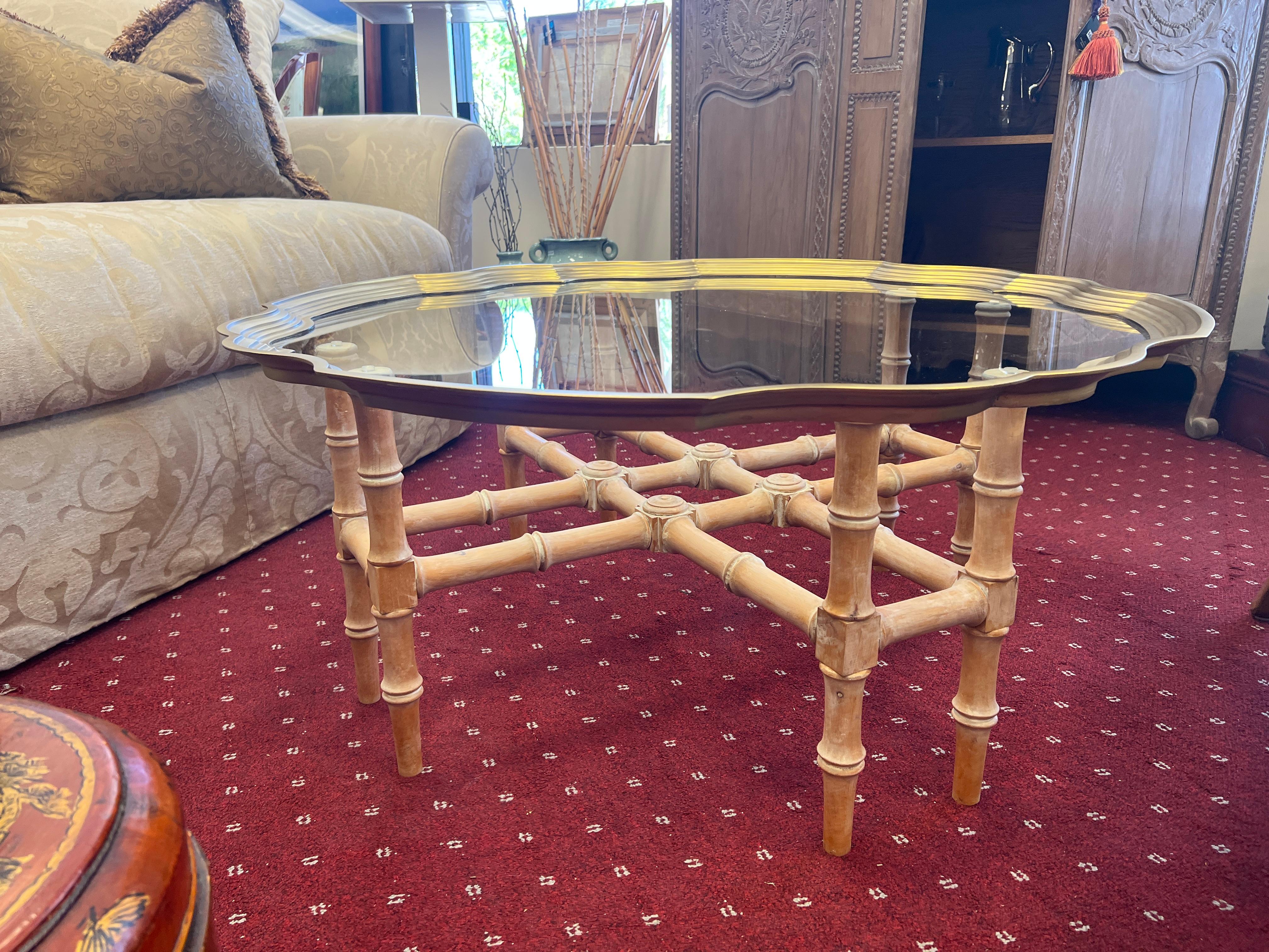 A Hollywood Regency Brass & Glass Cocktail  Tray Table on a Faux Bamboo Wood Base.  The table features a trestle form base made of wood, finished in a white-wash tone. The glass tray top features a solid brass scalloped edge, providing a practical