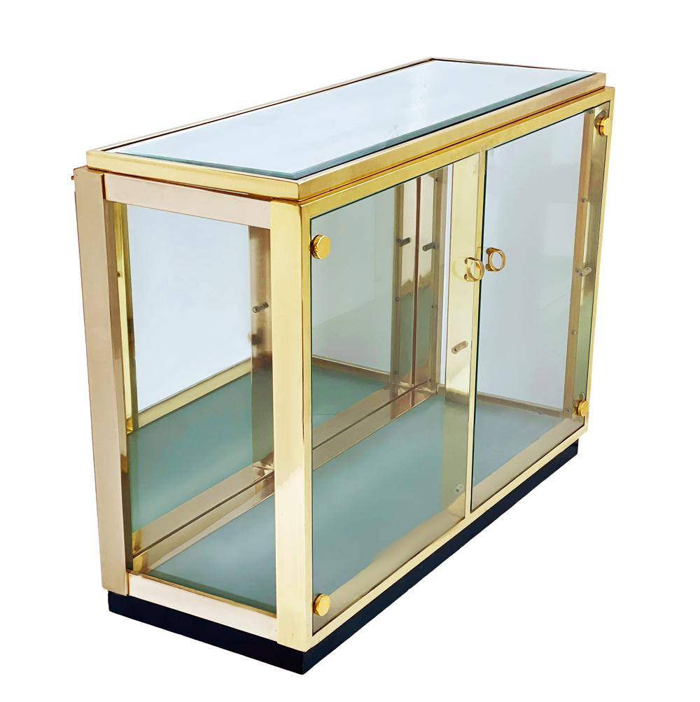 A sleek & modern display cabinet from Italy circa 1970s. It features mirrored top and back with glass door and sides. The brass framing is bright & shiny. The bottom lights up but looks great without the light on. There are two glass shelves that