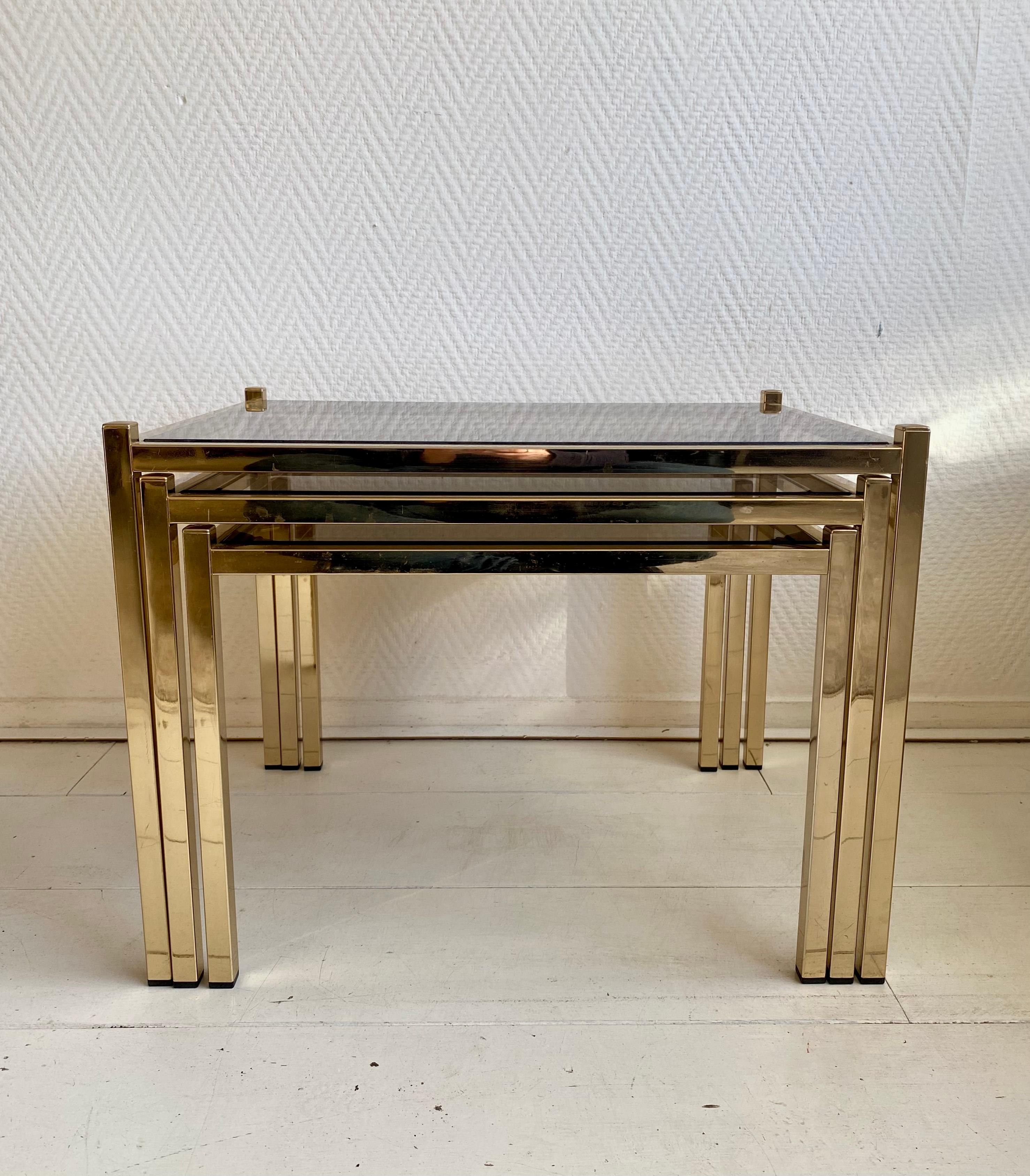 Set of three European 20th century brass and Smoked glass Nesting tables. The set has a warm and rich appearance with normal/light wear for their age. 