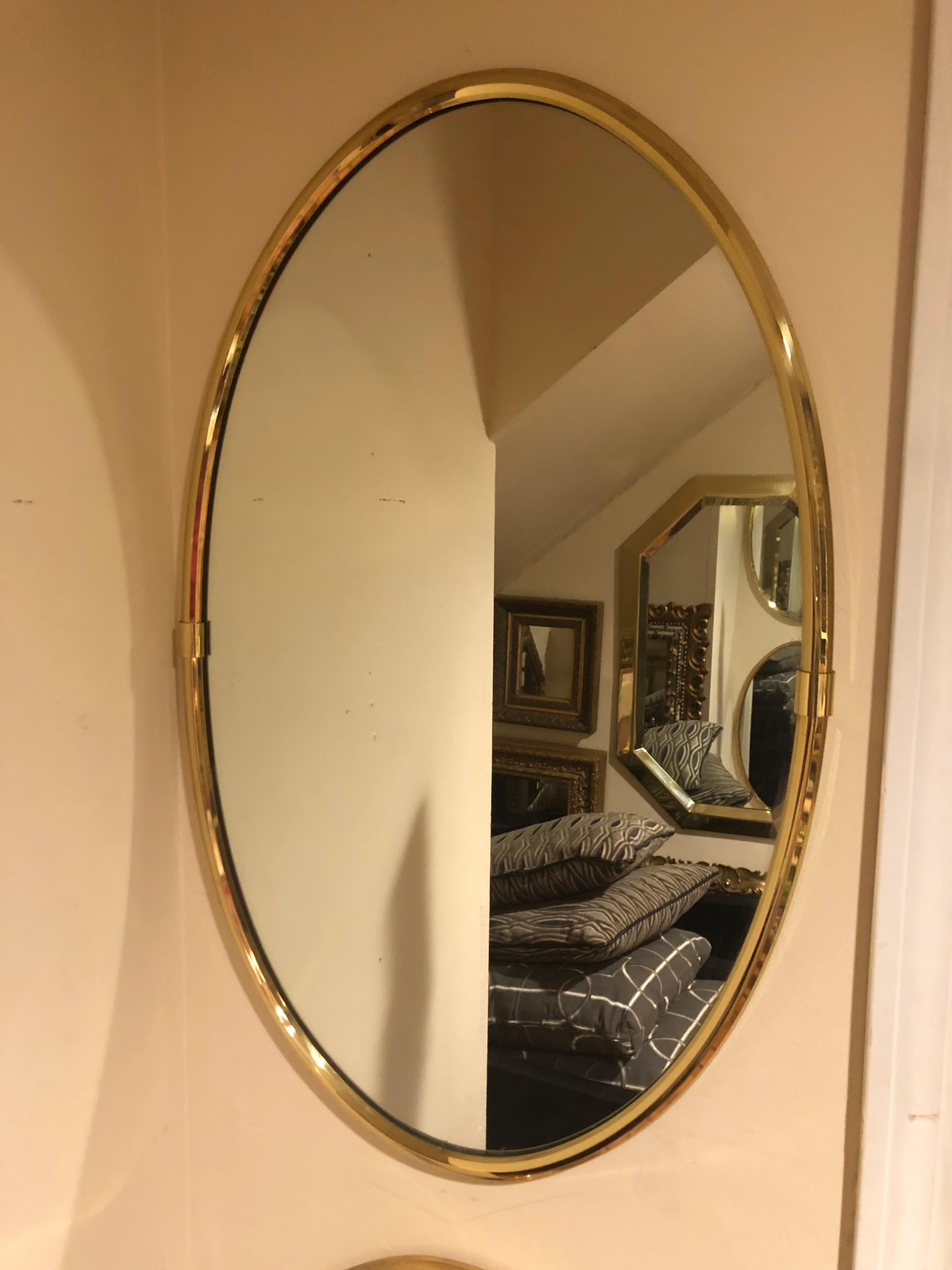 Hollywood Regency brass oval mirror. Most likely Italian. Banded, beveled edge to the brass frame. Simple, elegent lines with a small band in the middle on either side. The mirror is the top one of the two. They are both the same size. Only this one