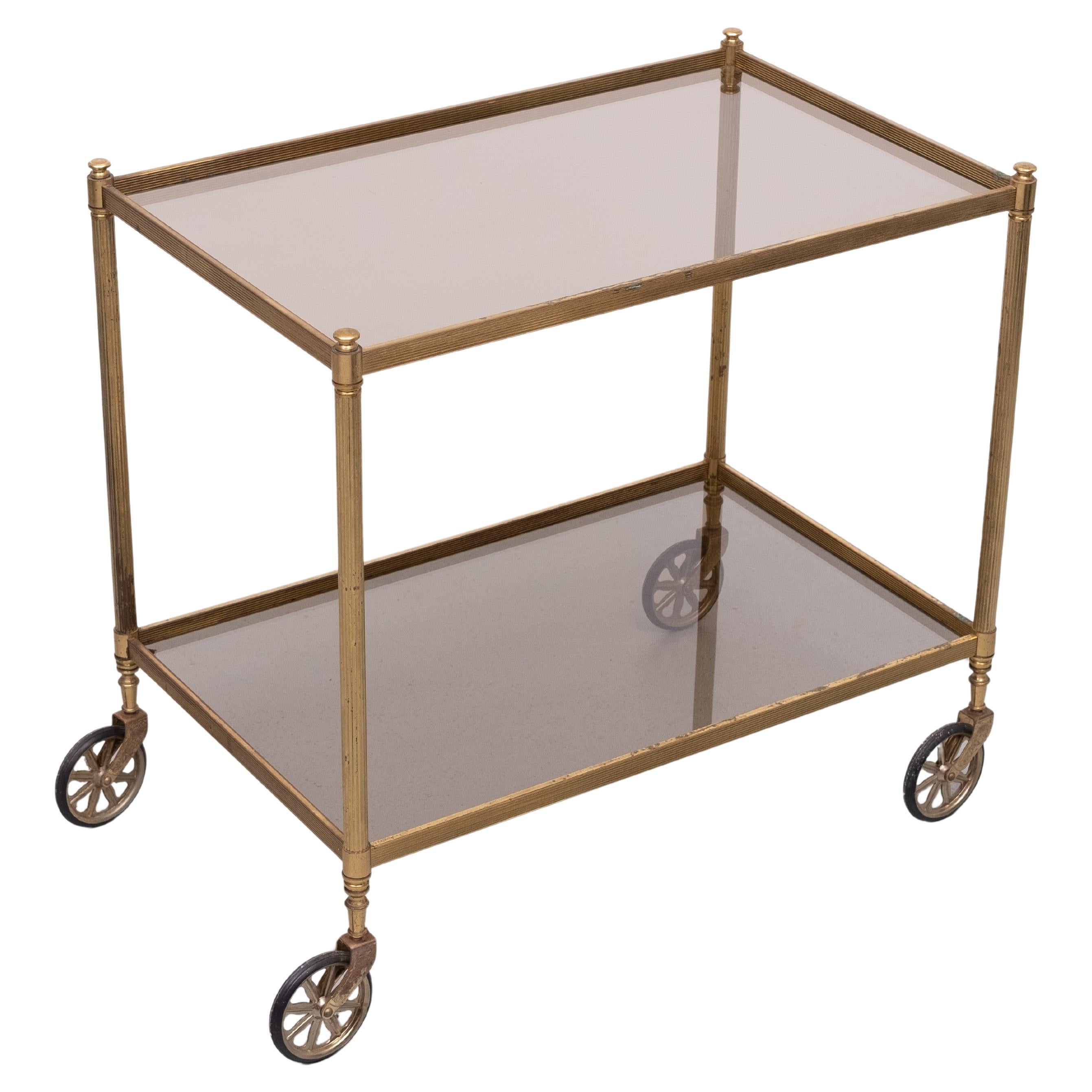 Magnifique chariot de service en laiton, livré avec son emballage d'origine. 
Dessus en verre fumé brun . sur roues  Beaucoup de patine sur le laiton,
Attribué à la Maison Jansen . 1970s 