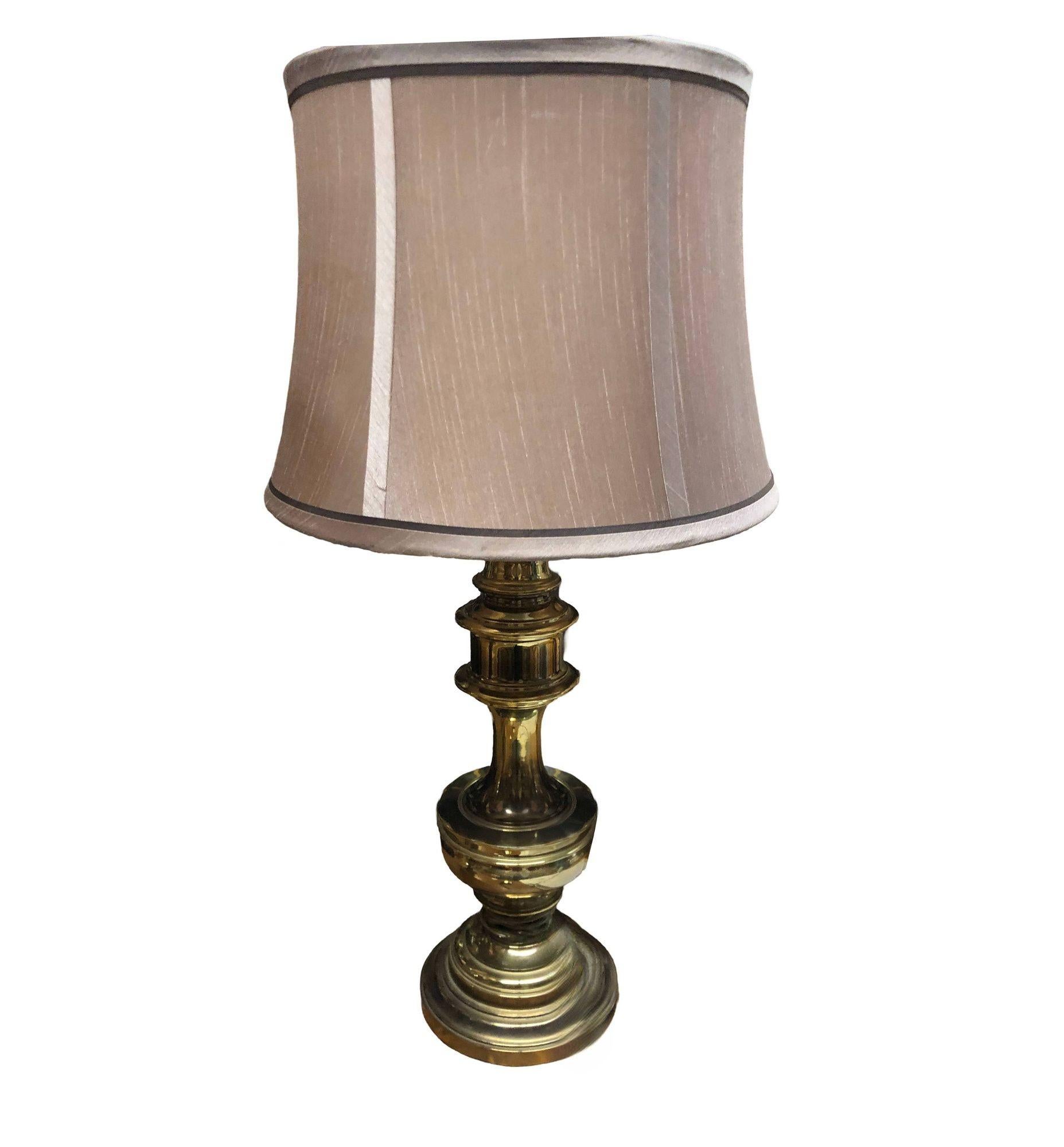 Hollywood Regency Brass Stiffel Style Table Lamp w/ Shade featuring a bright sealed brass finish with tan color fabric shade. Illuminate your space with a touch of classic elegance! This mid-century vintage table lamp features a sleek design and a