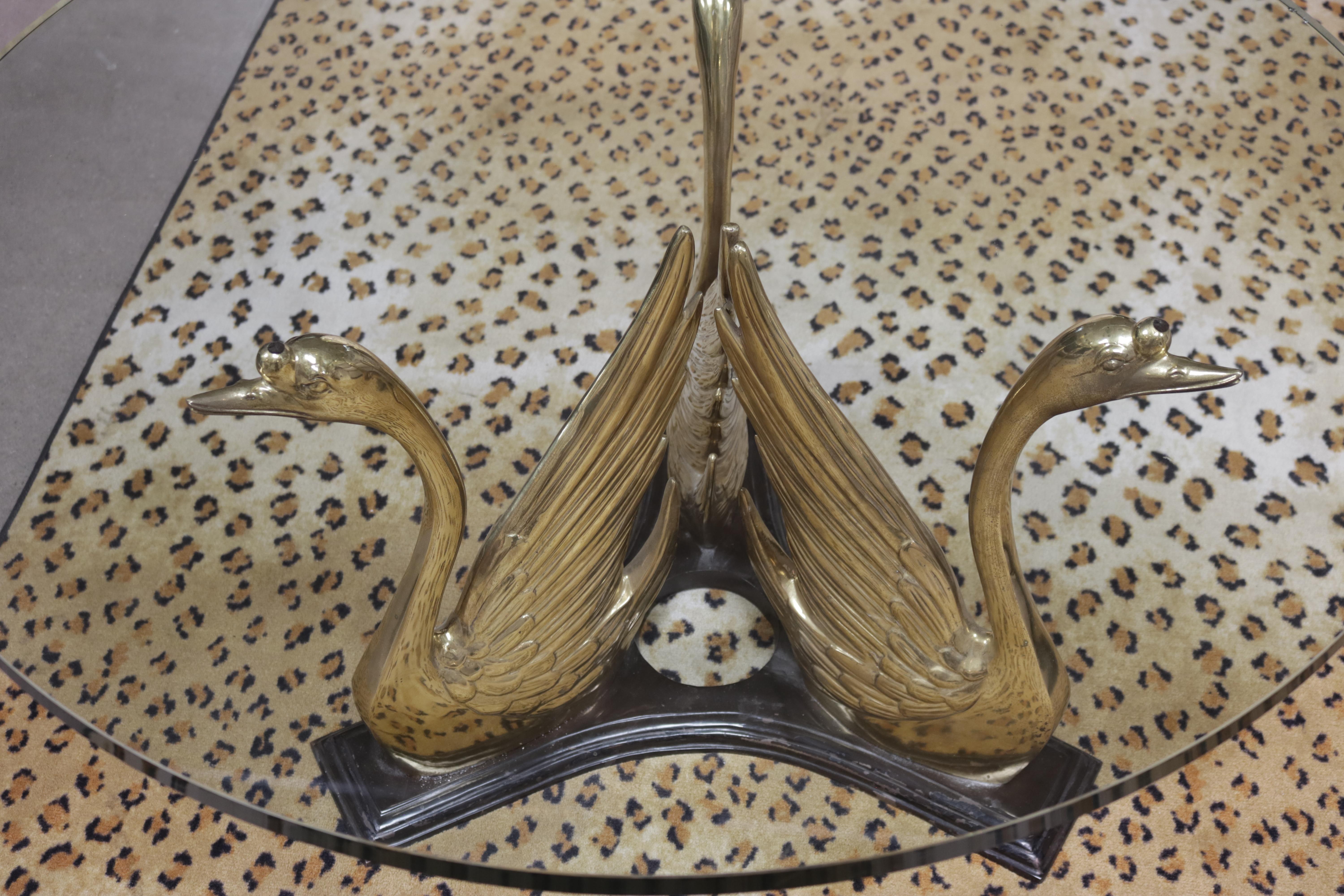 Im Stil von Maison Jansen trägt eine Schar von drei Schwänen aus Messing eine runde Glasplatte und bildet so einen eleganten Cocktailtisch. Sie sind an einem Sternfuß aus schwarz lackiertem Messing befestigt. Das Design der Schwäne ist den Motiven