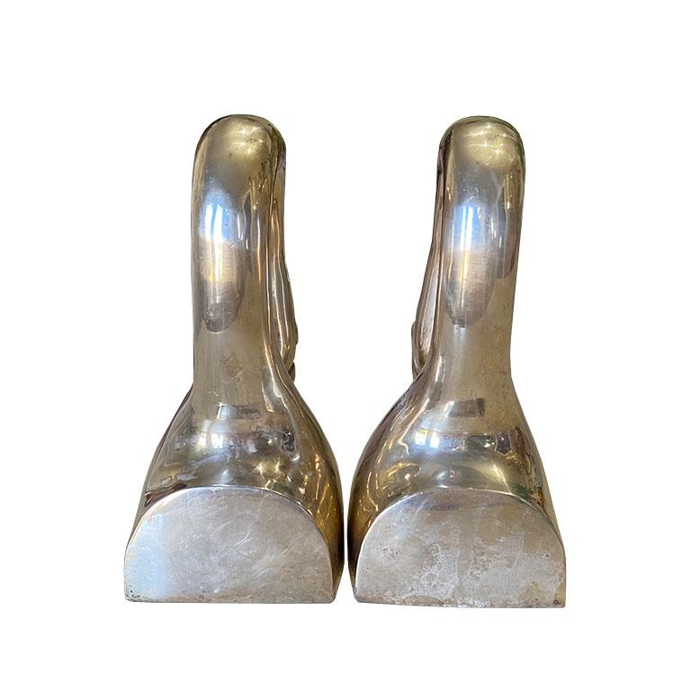 A pair of Hollywood Regency brass swan bookends. In fabulous vintage condition, this pair is created from brass, and depict a swan with the beak to his chest. This set will be a fantastic addition to any midcentury decor lover's bookshelf.