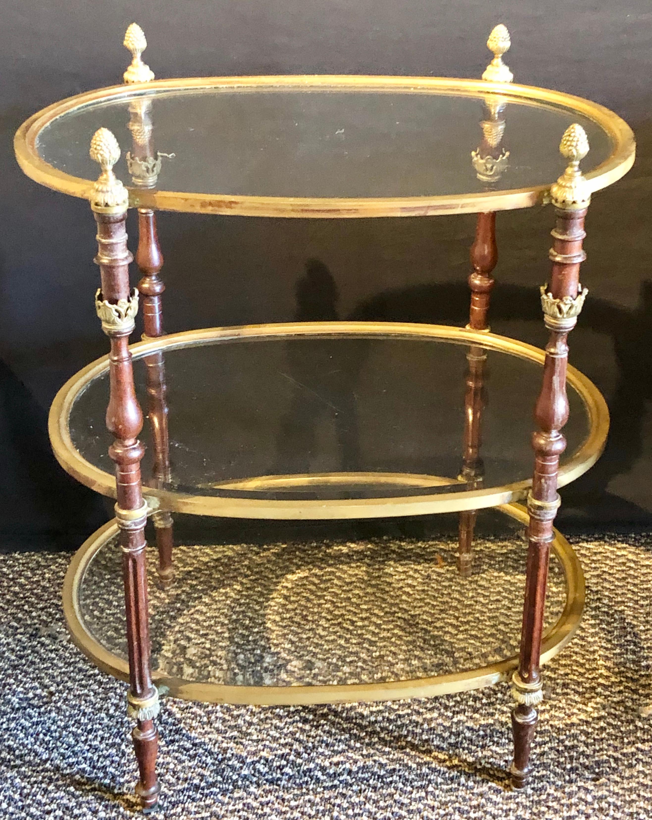 A three-tier bronze and mahogany beveled glass dessert stand in the manner of Maison Jansen. The burgundy colored column form sides terminating in bronze finials supporting three oval glass bronze framed shelves making for a lovely display.
