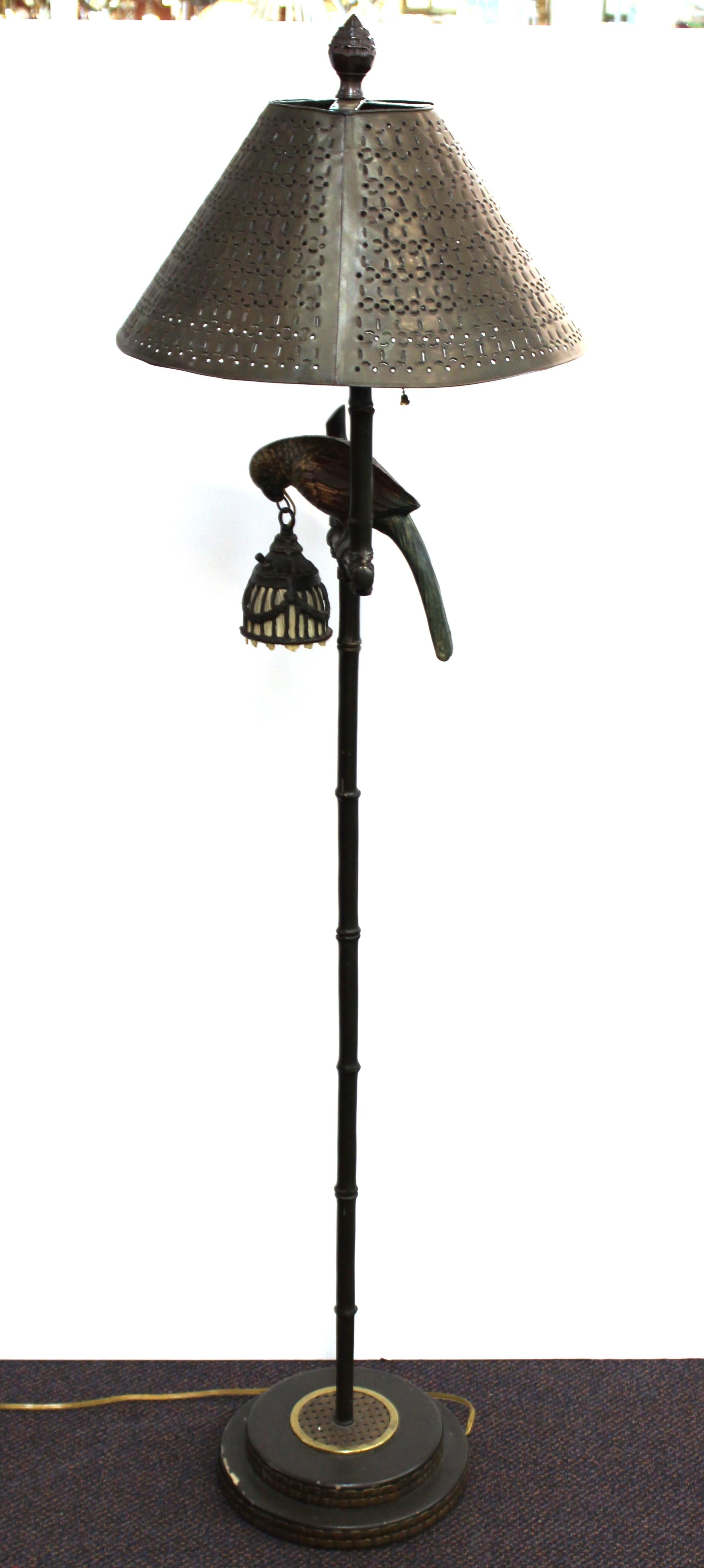 Hollywood Regency bronze floor lamp with a parrot on his perch, holding a smaller hanging reading lamp in his beak. Metal perforated shade and fabric interior shade for the reading lamp. The piece is in great vintage condition.