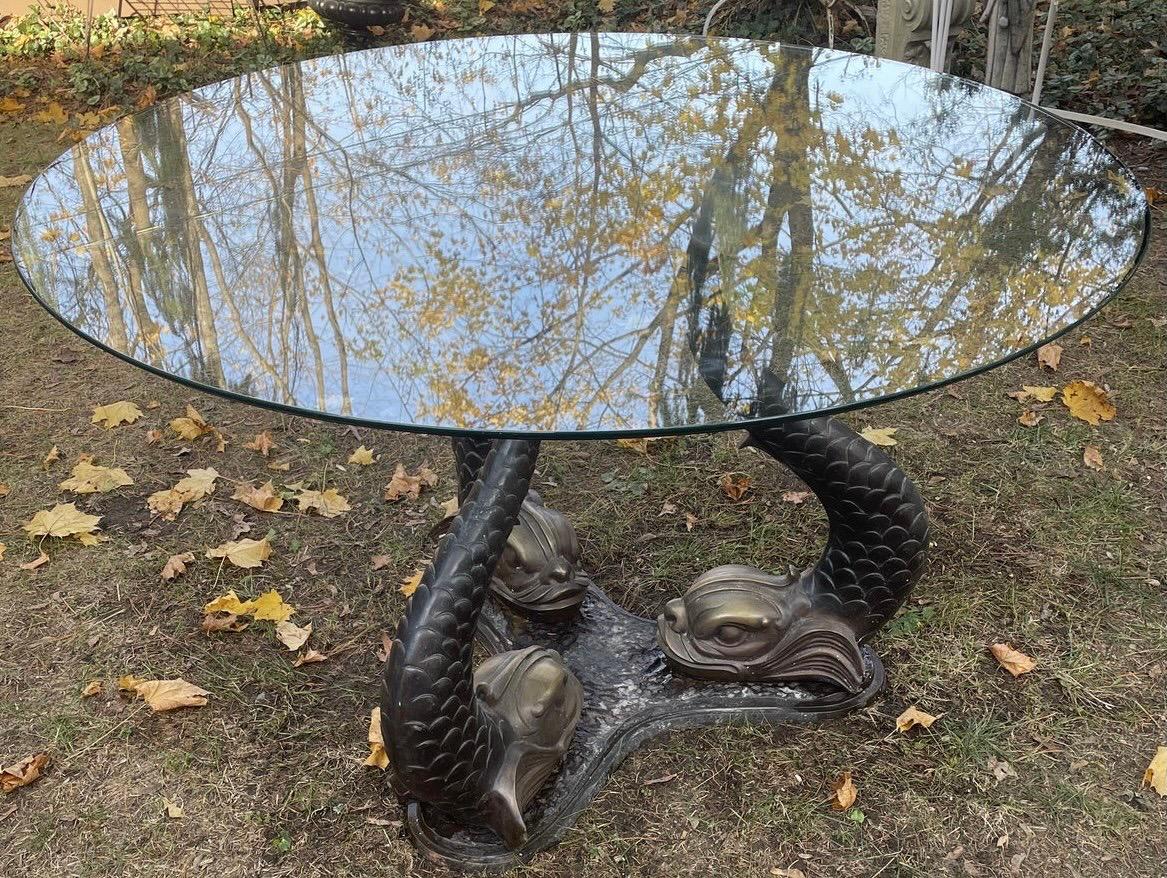 Magnificent heavy bronze sculptural center table with glass top that sits on three separate carved bronze dolphins that fit into a single bronze base. Dolphins can be reconfigured to face in or out. An iconic Hollywood Regency architectural gem.