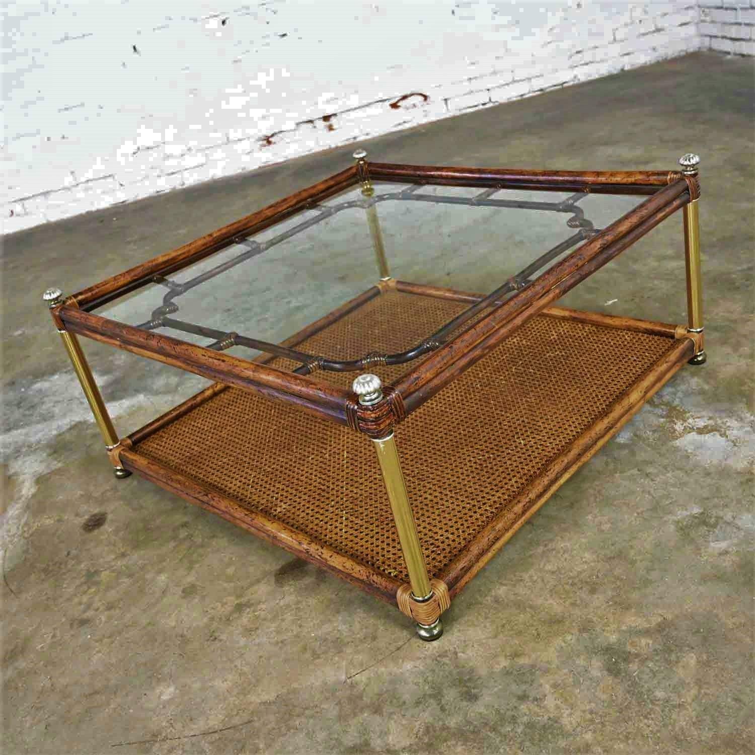 Lovely Hollywood Regency, Campaign, and/or Chinoiserie style faux bamboo, cane, and glass top coffee table. Comprised of a dark stained wood frame, silver and brass tone accents, rattan wrappings, cane bottom shelf, faux bamboo look designs, and a