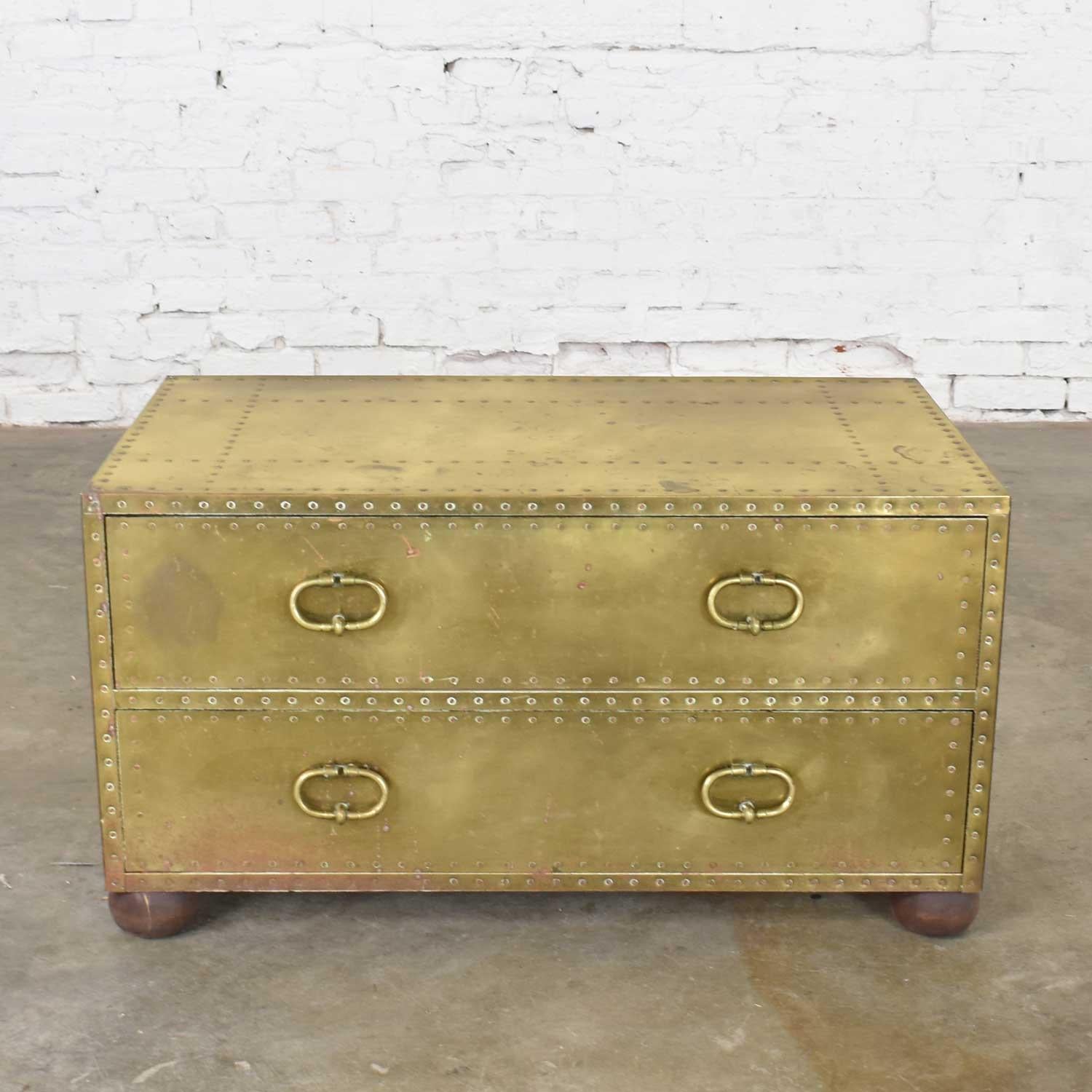 Awesome two-drawer brass-clad chest in a Hollywood Regency Campaign style by Sarreid Ltd., Spain. It is in wonderful vintage condition with a beautiful age patina to the brass including dings, dents, and color differences. The original wood bun feet