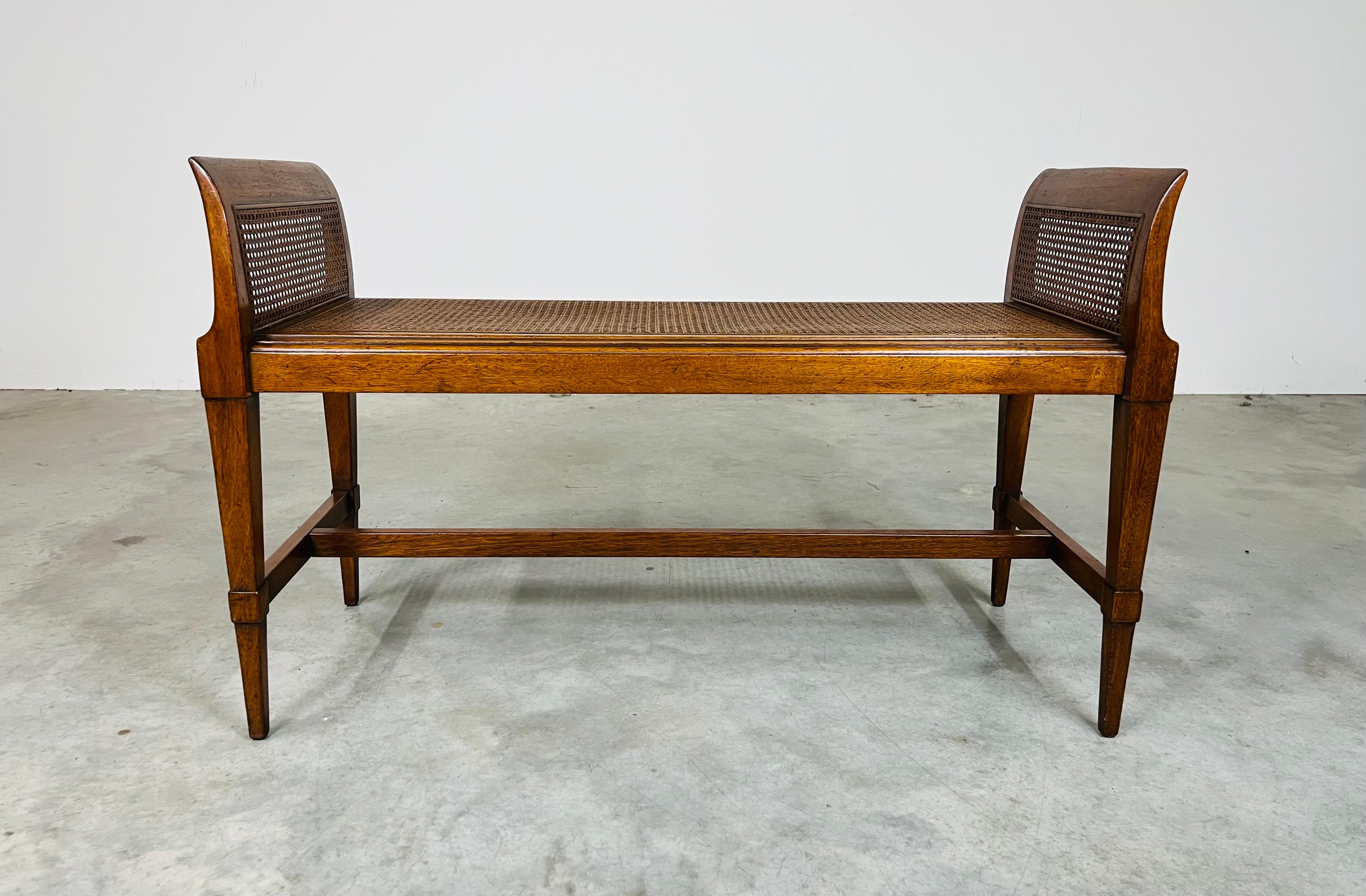 An elegant Mid-century cane window bench having hand carved mahogany frame in the Hollywood Regency style circa 1950. The cane is strong and in beautiful condition having no damage. The frame is solid, has been professionally cleaned and is ready