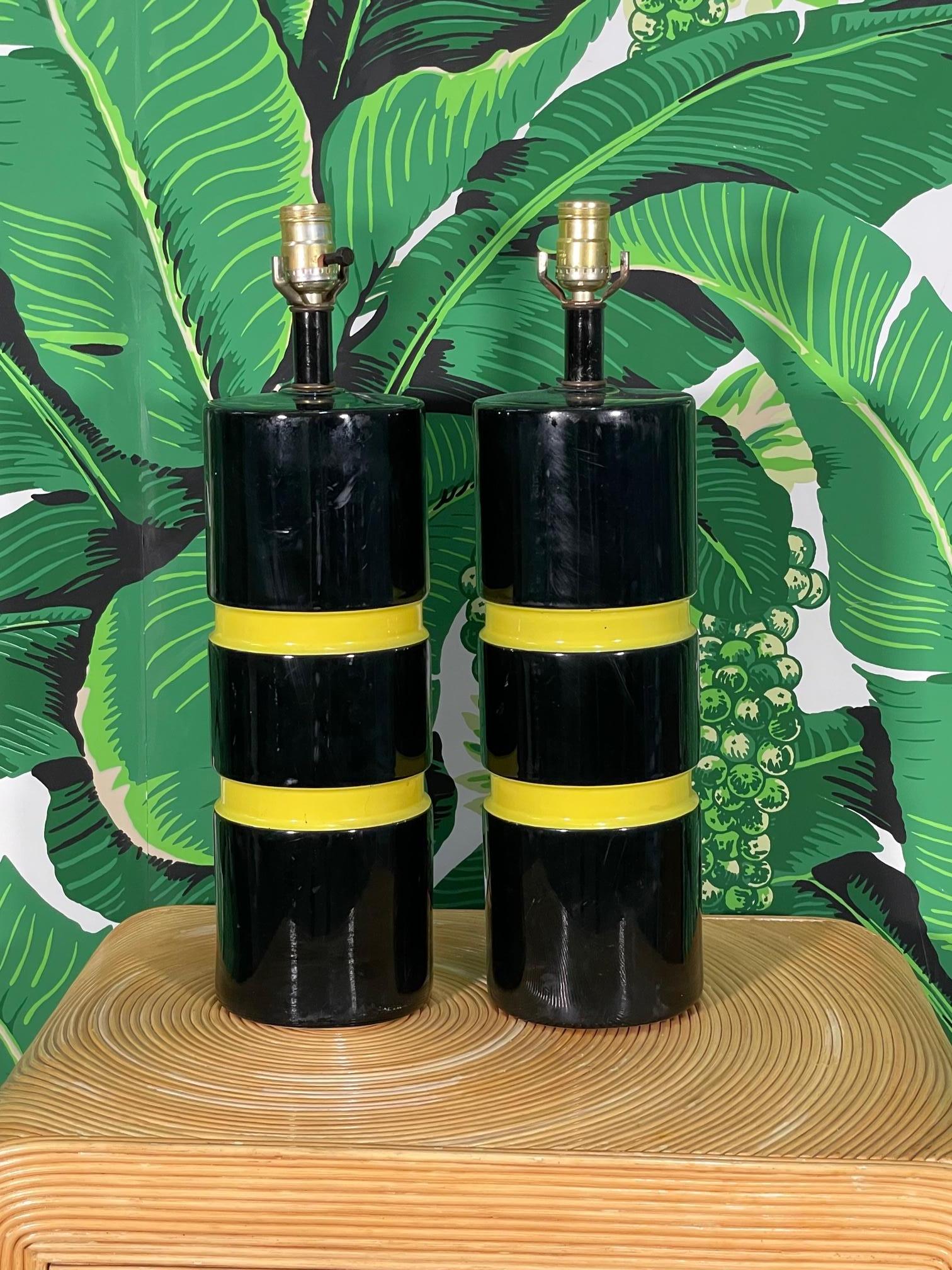 Pair of Hollywood Regency style table lamps feature a ceramic body in gloss black with horizontal bands of yellow insets. Good condition with minor imperfections consistent with age, see photos for condition details.

