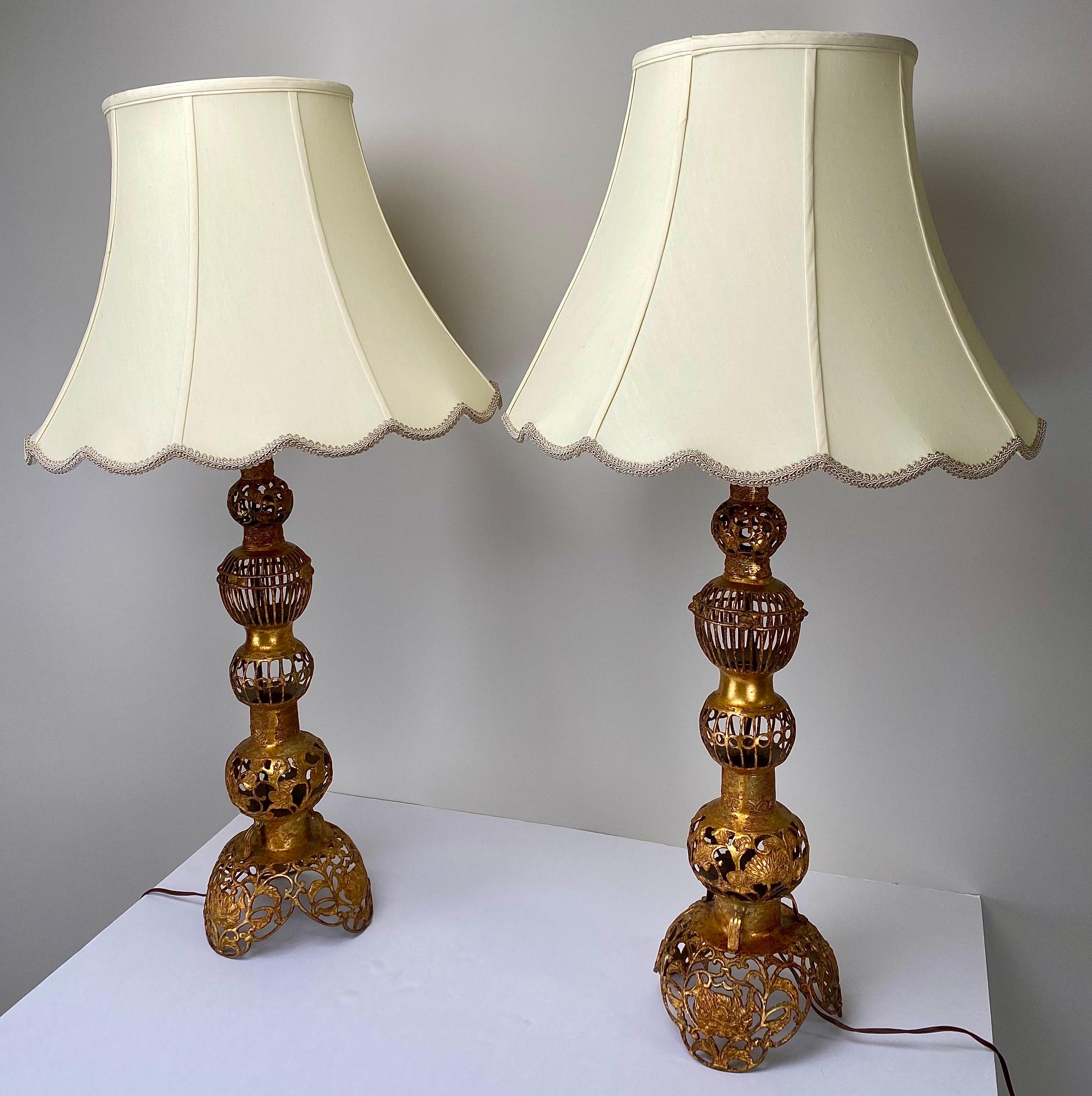 A striking pair of Hollywood Regency Chinese-style table lamps, exuding opulence and grace. Crafted with meticulous artistry, these tiered lamps stand as majestic pieces, fashioned from bronze and bathed in a luxurious copper hue. The intricate