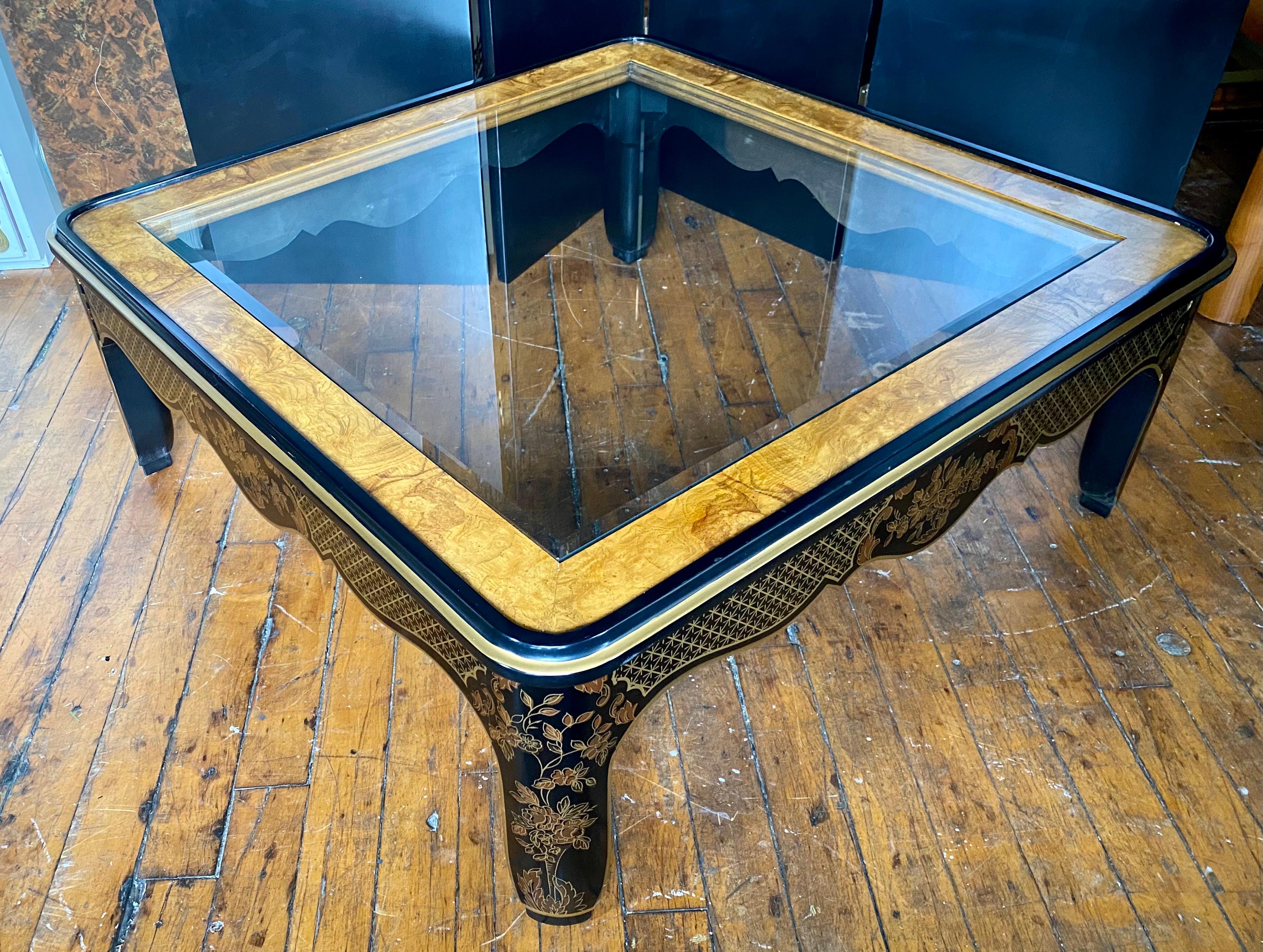 Large square Hollywood Regency style burl wood and glass coffee table by Drexel Furniture. This sculptural cocktail table features original gloss black wood frame with hand painted gold leaf detailing of fretwork and floral design. Includes original