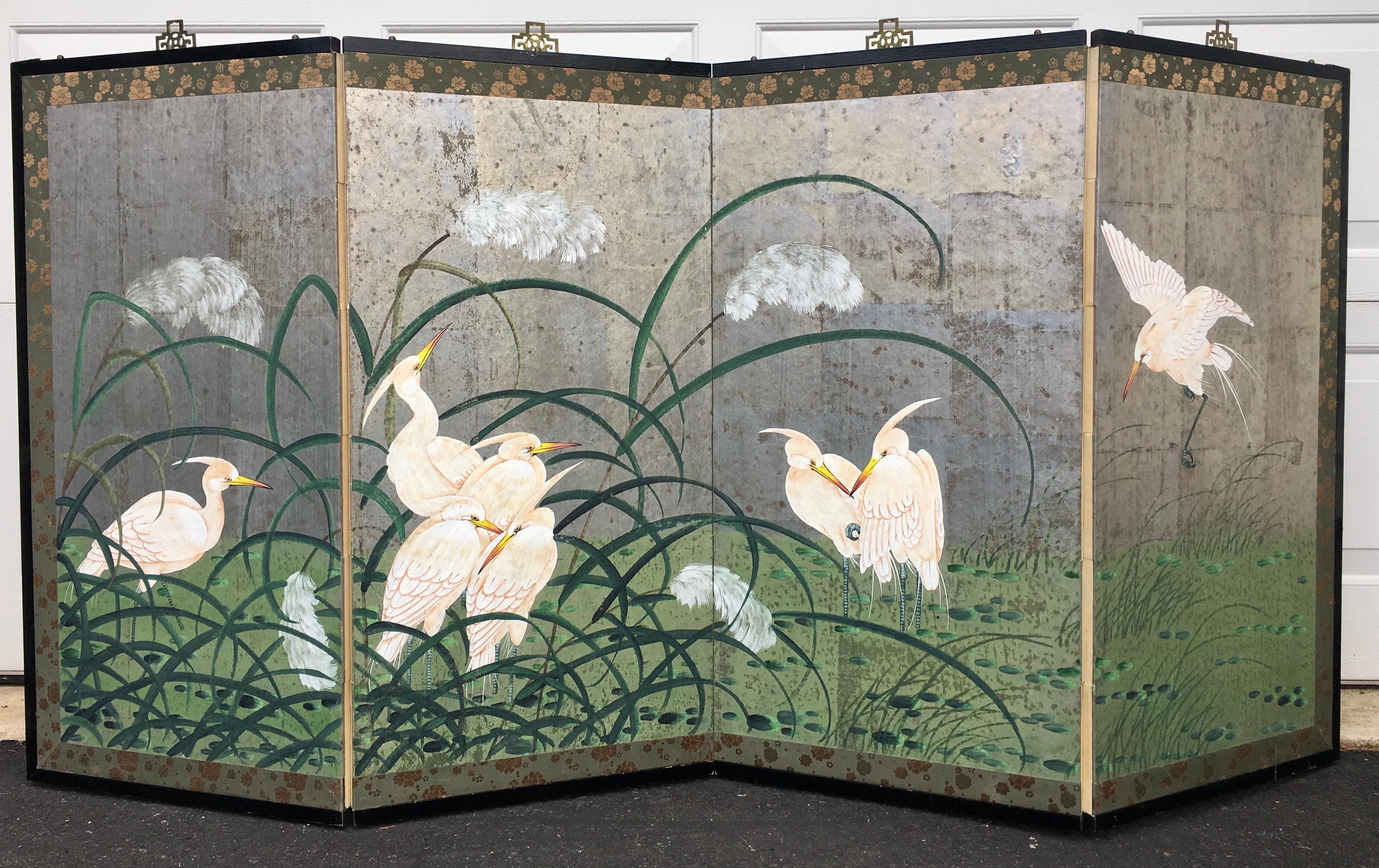 Hollywood Regency Chinoiserie style four panel folding wall or floor screen. This Japanese painting/ art wall hanging features a silver leaf finish with heron crane birds. Black wood frame is bordered by silk brocade trim with brass hardware.