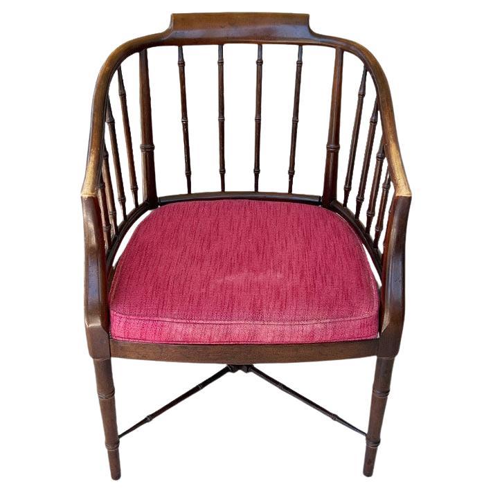 A stunning traditional Chinoiserie Chippendale faux bamboo tub chair in the manner of Baker Furniture Company. This solid wood barrel back tub chair is created from wood and has a red box cushion seat with piping around the edges. The lines of this