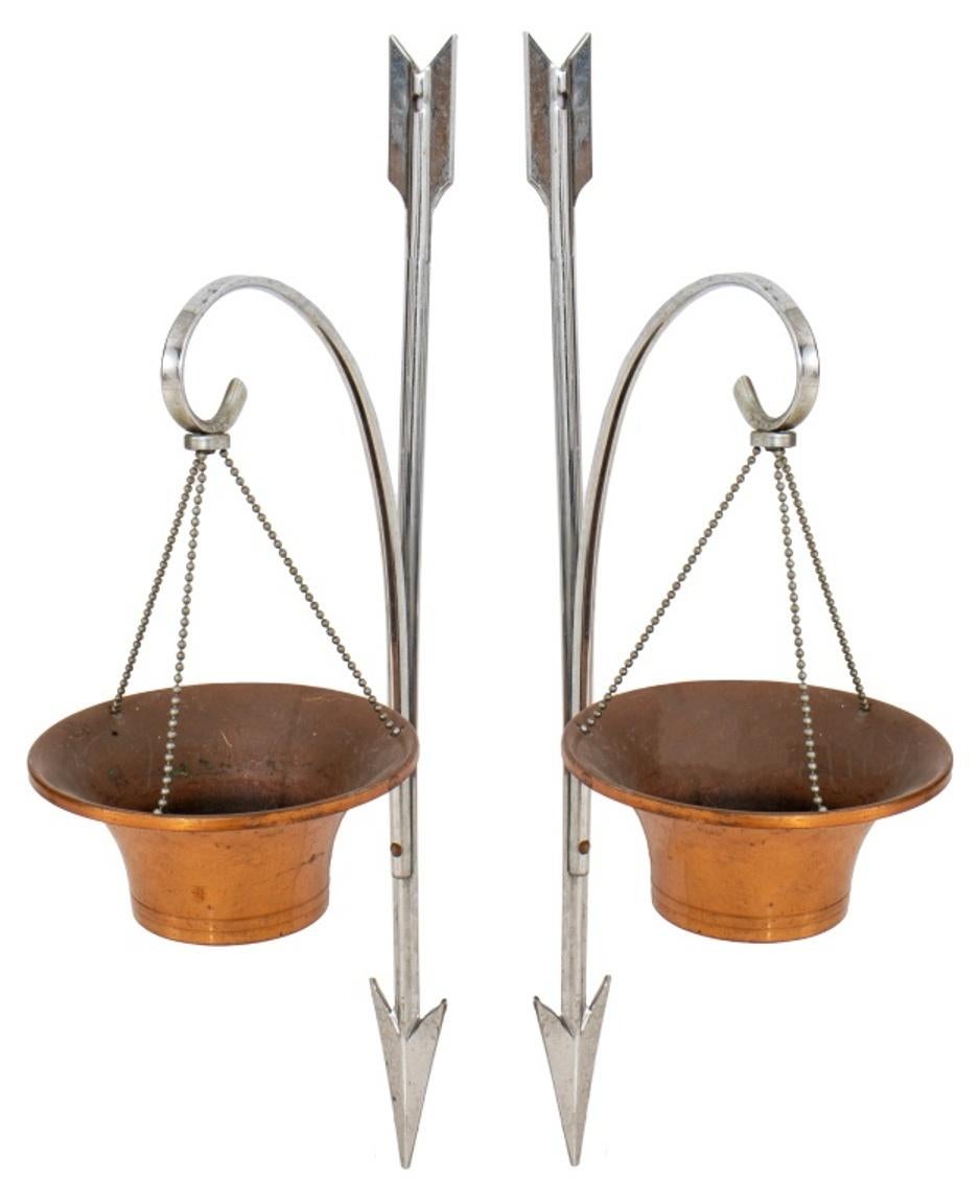 Pair of Hollywood Regency chrome & copper votive appliques or hanging planters, in the form of inverted chrome arrows issuing a bracket supporting a small copper basket for a votive light. In good vintage condition.

Dealer: S138XX