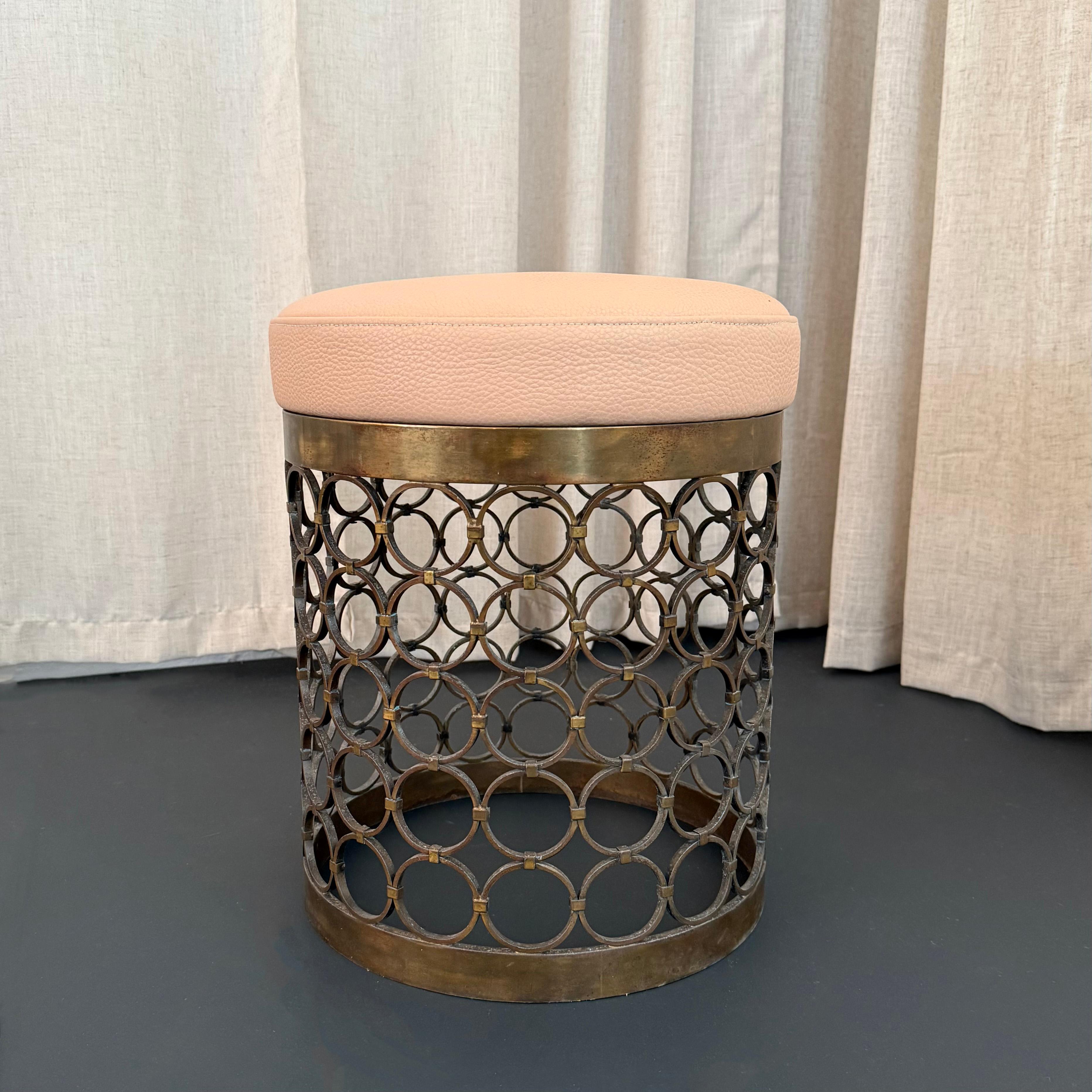 Ce tabouret ou ottoman séduisant du milieu du siècle, de style Hollywood Regency, est de forme cylindrique et utilise un motif circulaire comme élément clé du design. Le cadre en laiton massif patiné présente un motif circulaire répétitif qui attire