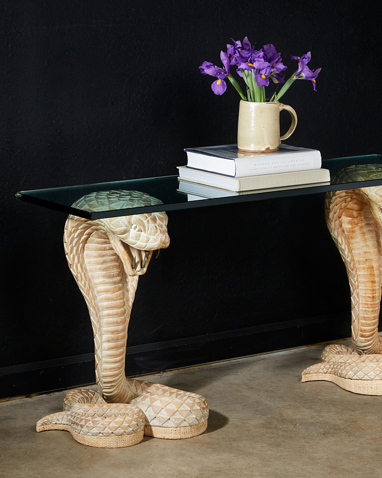 Dramatic console table featuring a pair of hand carved cobra snakes depicted in coiled striking positions. Topped with a pane of thick glass which was added later. Originally the snake bases had a Lucite top. Each snake has long brass fangs in its