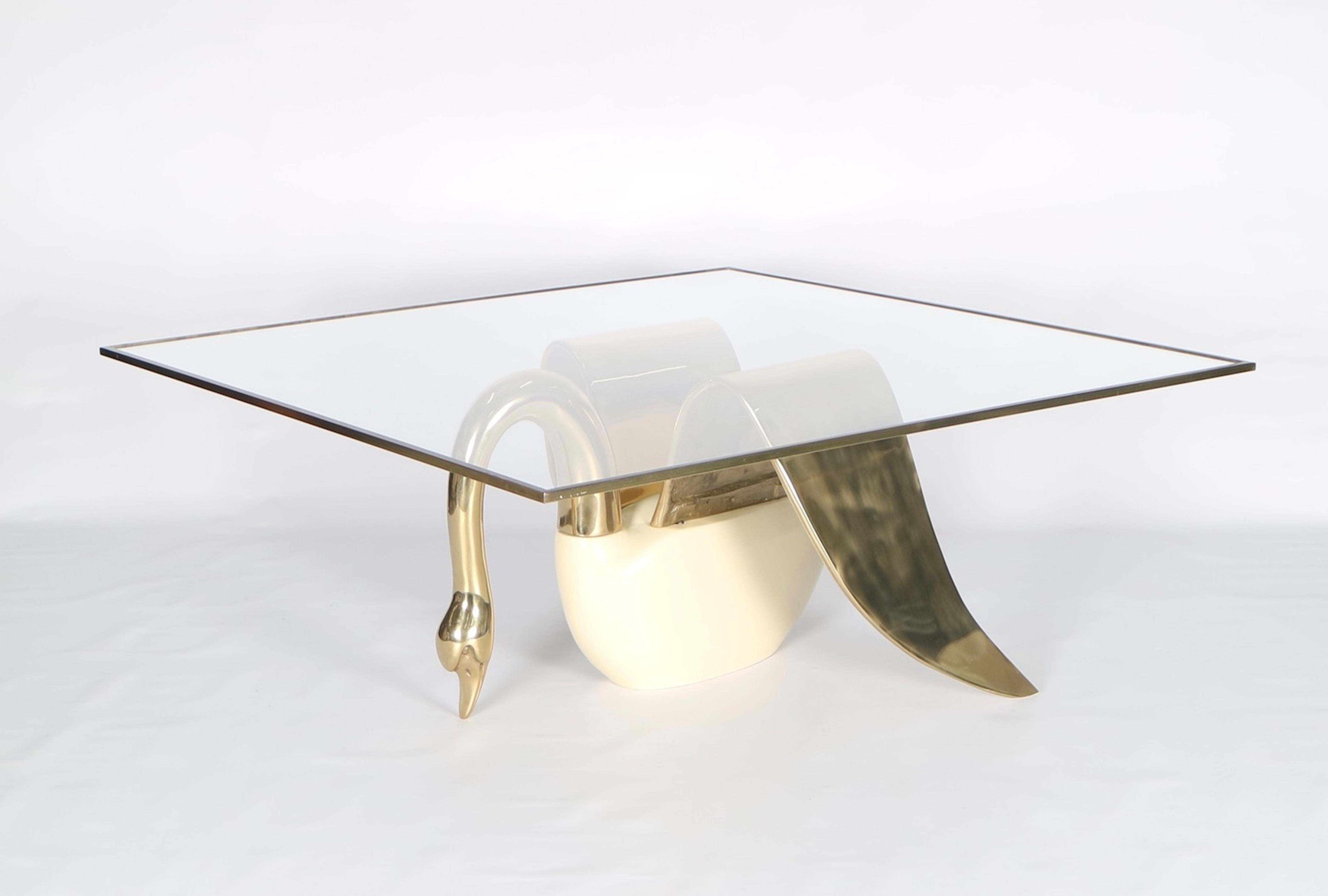 Hollywood Regency swan cocktail or coffee table in brass. Crafted in solid brass with lacquer wood body and square glass top with brass edges. The piece features a sculptural base in the shape of a seated swan with outstretched wings. Wear