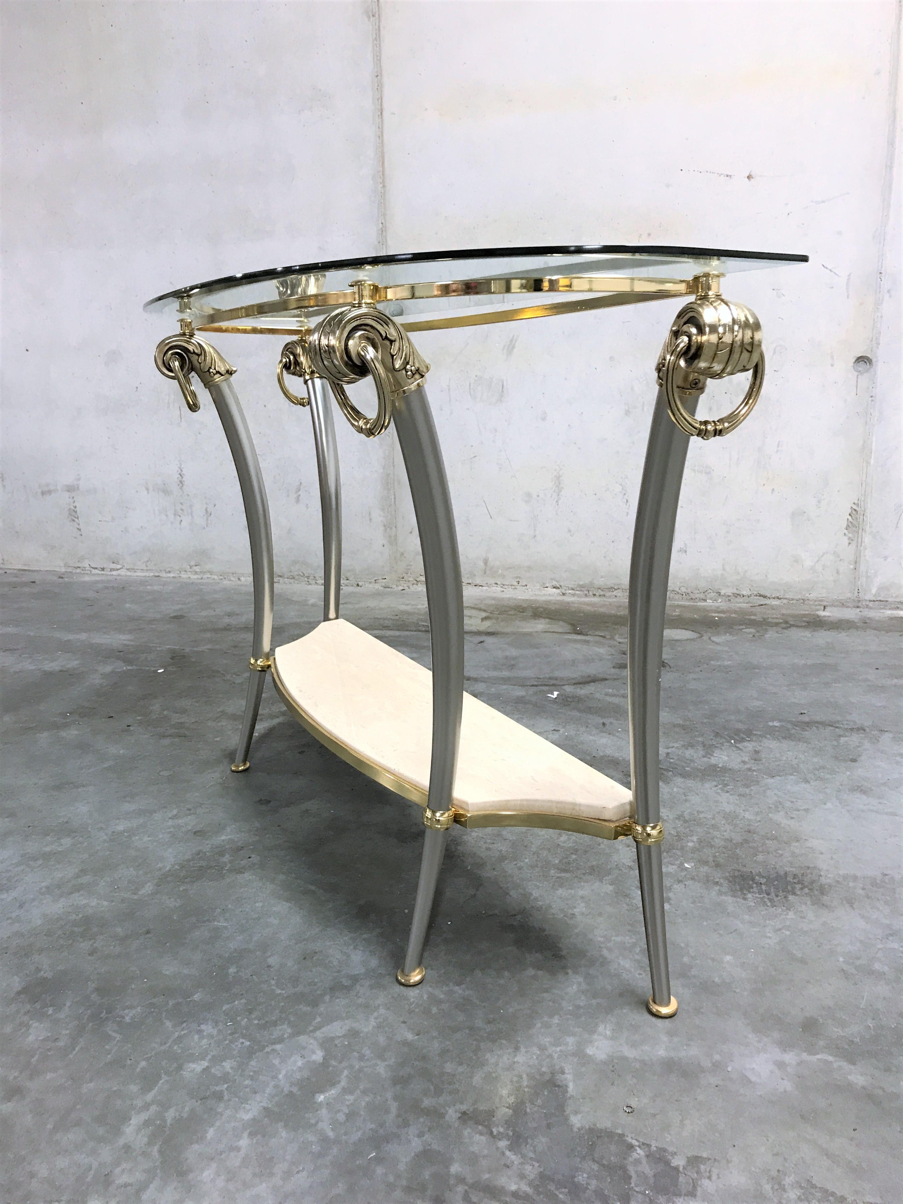Two-tier Hollywood Regency console table made from steel and brass with a beveled glass top and a travertine shelve.

Elegant bended legs and wide use of materials.

Very good condition.

1970s - Belgium

Dimensions:
Height