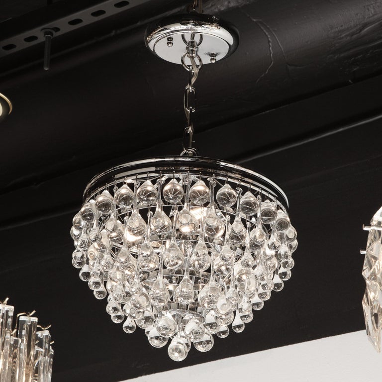 This stunning Hollywood Regency crystal teardrop chandelier features an abundance of hanging translucent glass tear drops suspended from a polished chrome frame consisting of six graduated concentric circular rows- imbuing the piece with a subtle