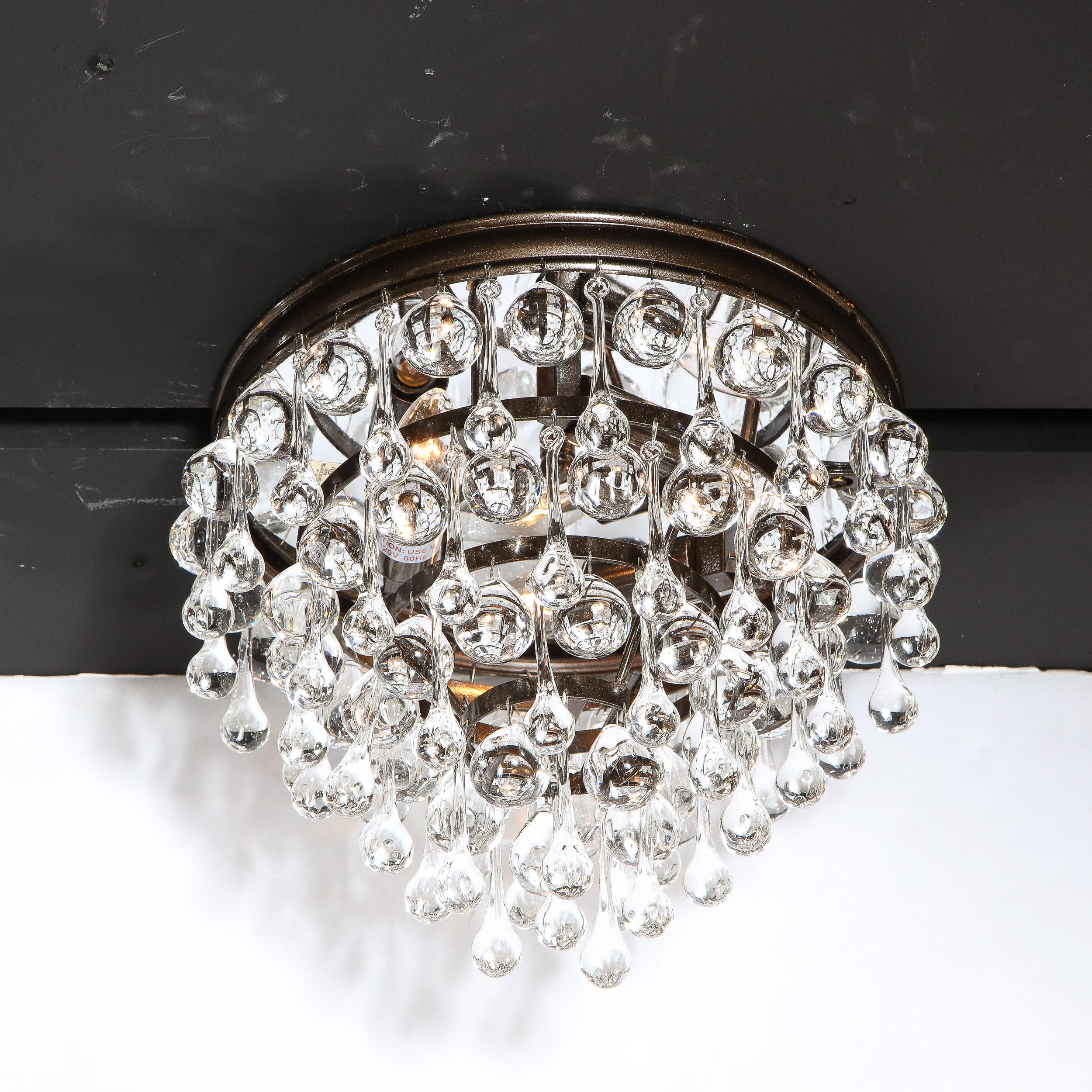 This stunning Hollywood Regency crystal teardrop flush mount chandelier features an abundance of hanging translucent glass tear drops suspended from a bronze frame consisting of six graduated concentric circular rows- imbuing the piece with a subtle