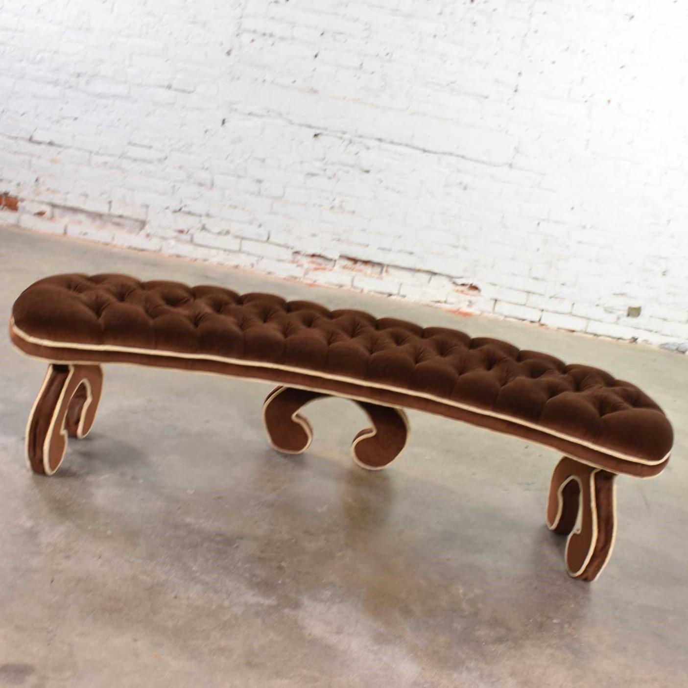 Amazing curved Hollywood Regency bench, which is fully upholstered, including its curved legs, and tufted in a cocoa brown velvet with contrasting welt. It is in wonderful vintage condition. It retains its original fabric so if you look closely, you