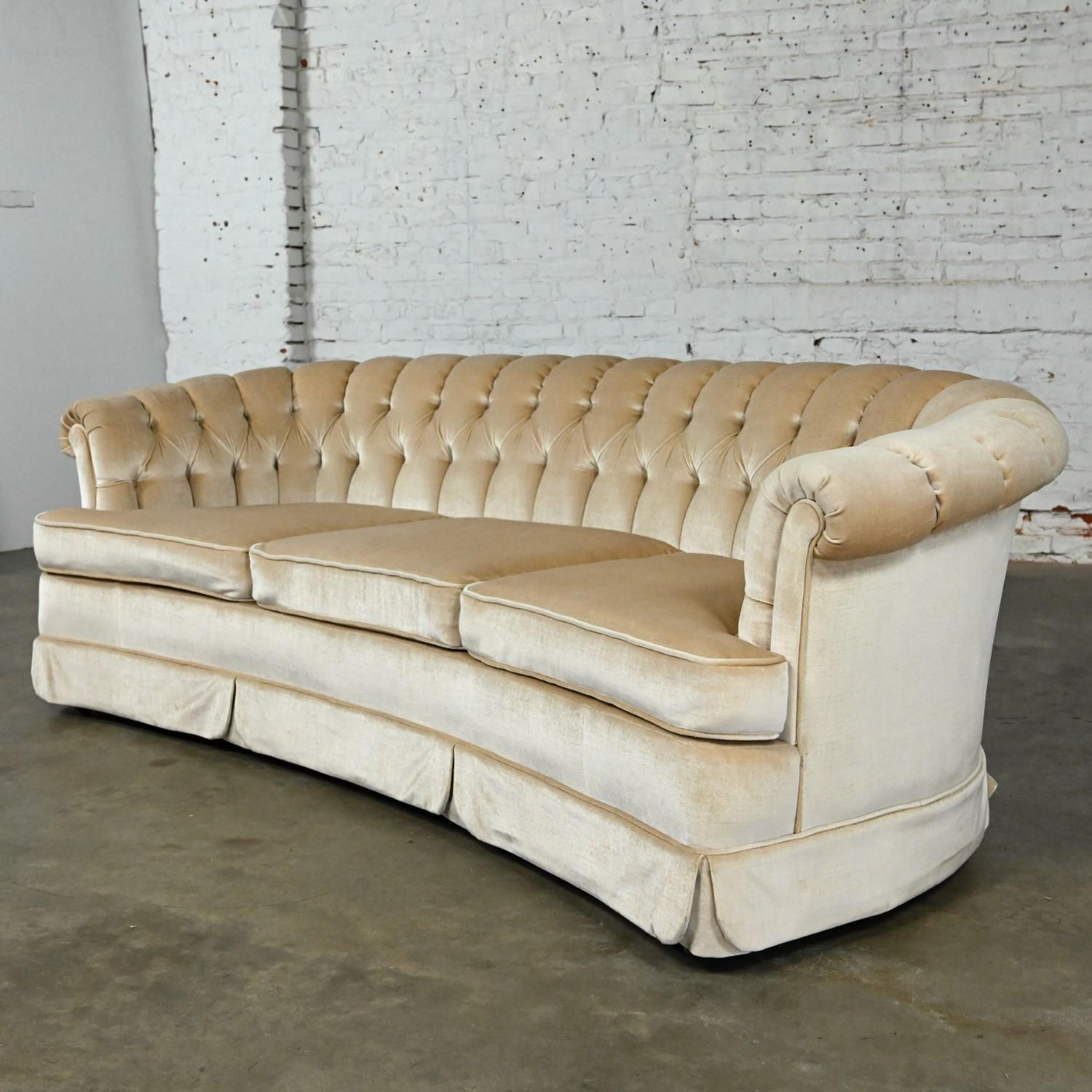 Lovely Mid-20th Century Hollywood Regency curved sofa by Lee Harvey for Maddox with beige or camel colored velvet fabric, rolled arms, button tufted & channeled back, three loose, zippered foam seat cushions, three ball casters in front & three