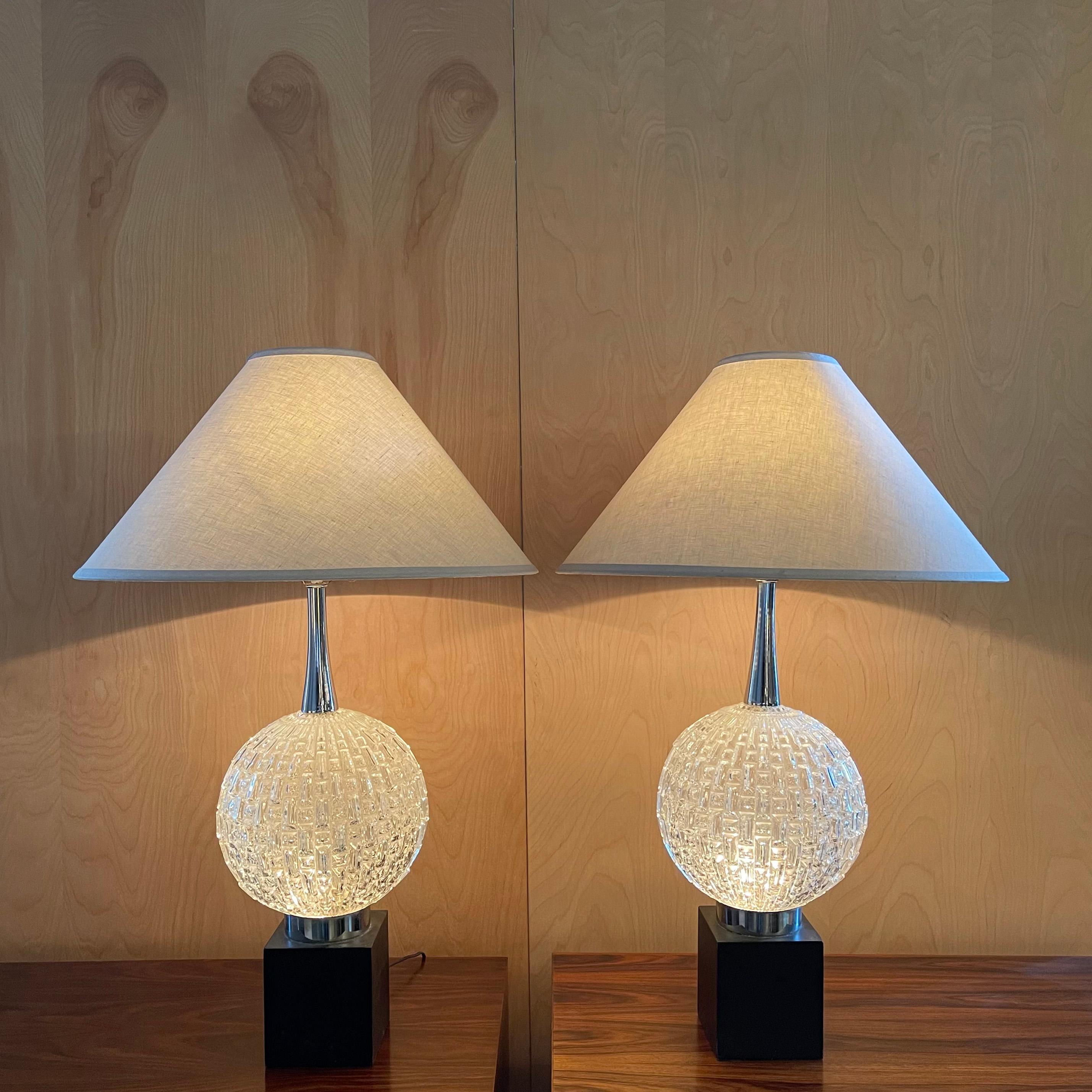 Pair of glamorous, Hollywood Regency, table lamps feature 10 inch diameter, cut glass globes that light up, atop painted steel cube bases with chrome necks. The lamps light 3 ways; on top, bottom and then together. The linen coolie shades measure 21