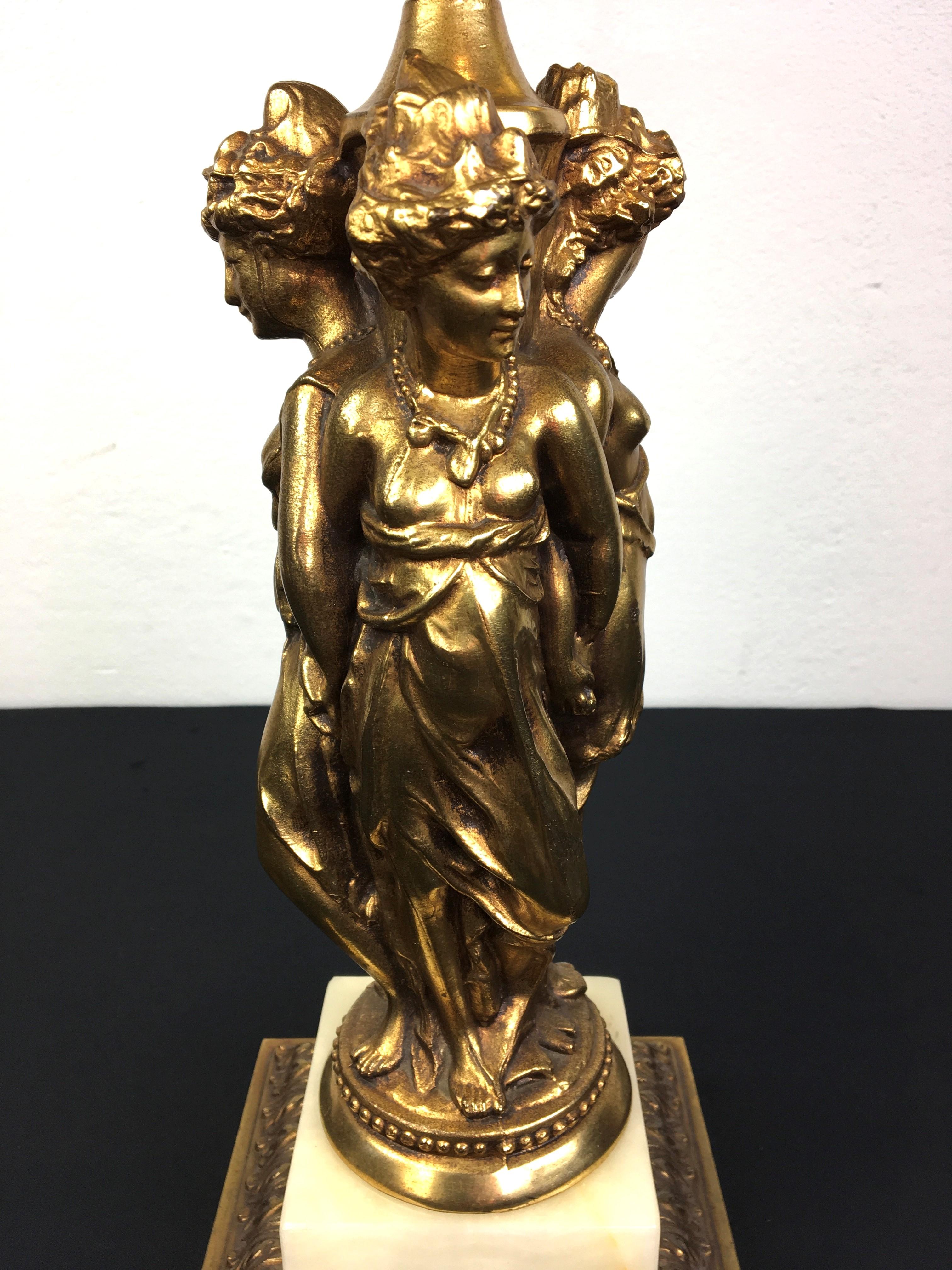 Hollywood Regency Deknudt Tischlampe mit einem eleganten Trio von Göttinnen oder Damen. Diese ikonische Göttin-Lampe ist ein Beispiel für großartiges, monumentales Design aus den 70er Jahren. Hergestellt vom belgischen Unternehmen für hochwertige