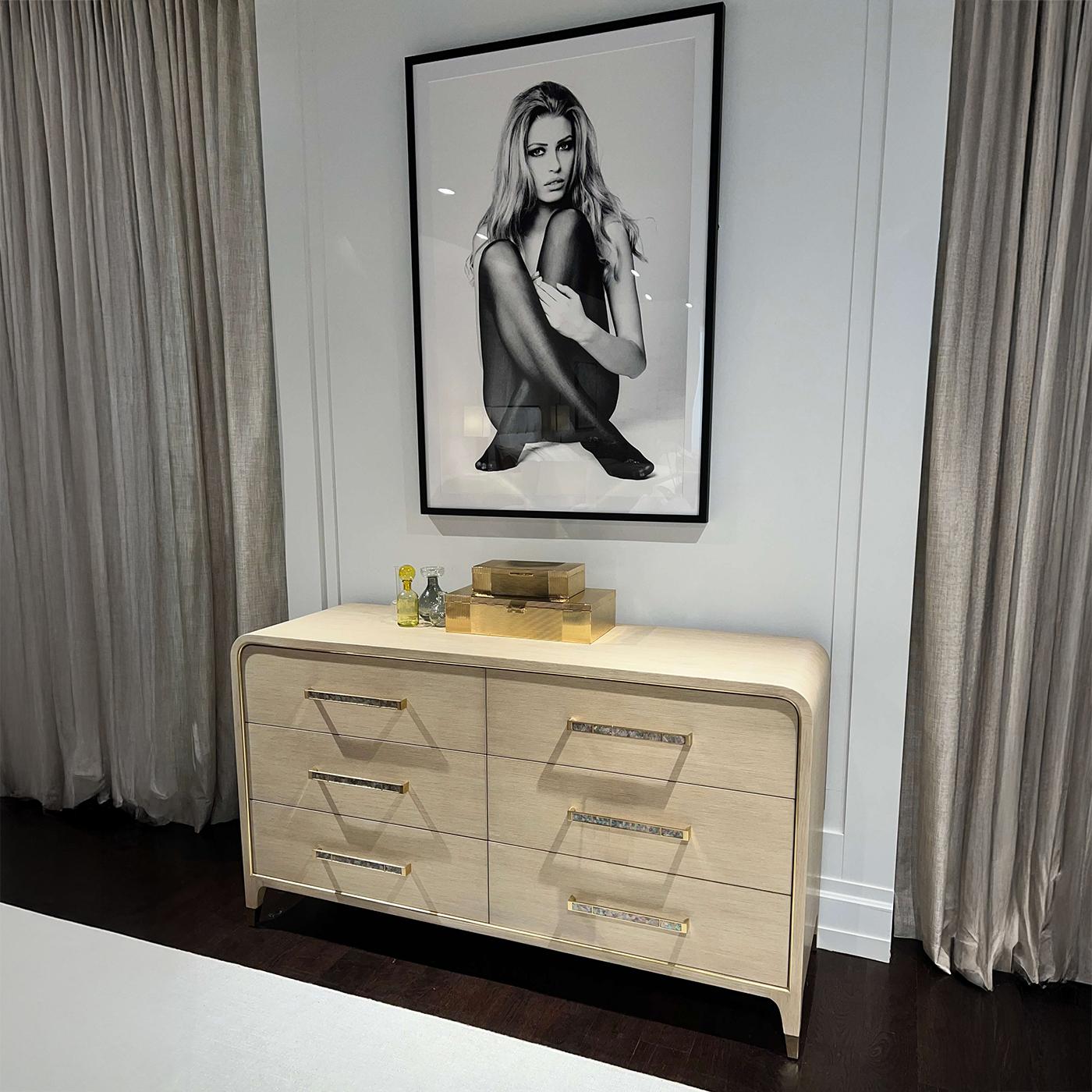 Meticulously artisan made, it serves as a luxurious statement piece for those who embrace an elegant approach to life. Shown in a light wood finish, the dresser features gracefully rounded edges framed with subtle brass inlay, exuding tailored