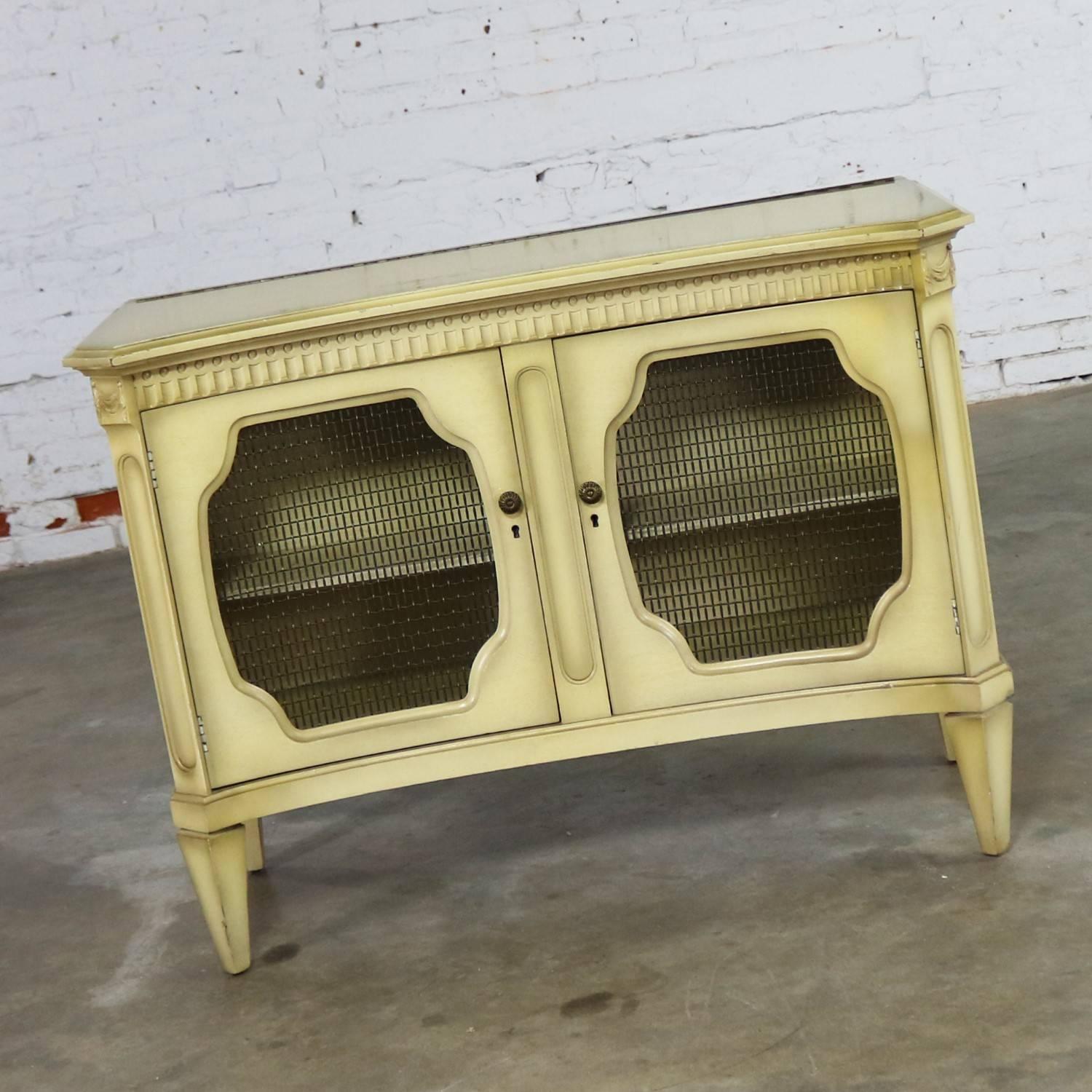 Elegant Hollywood Regency dry bar and liquor cabinet. This midcentury cabinet is done in a wonderful ivory painted finish called, according to the stamp on the back, Golden Glo. It is in beautiful vintage original condition and any appropriate