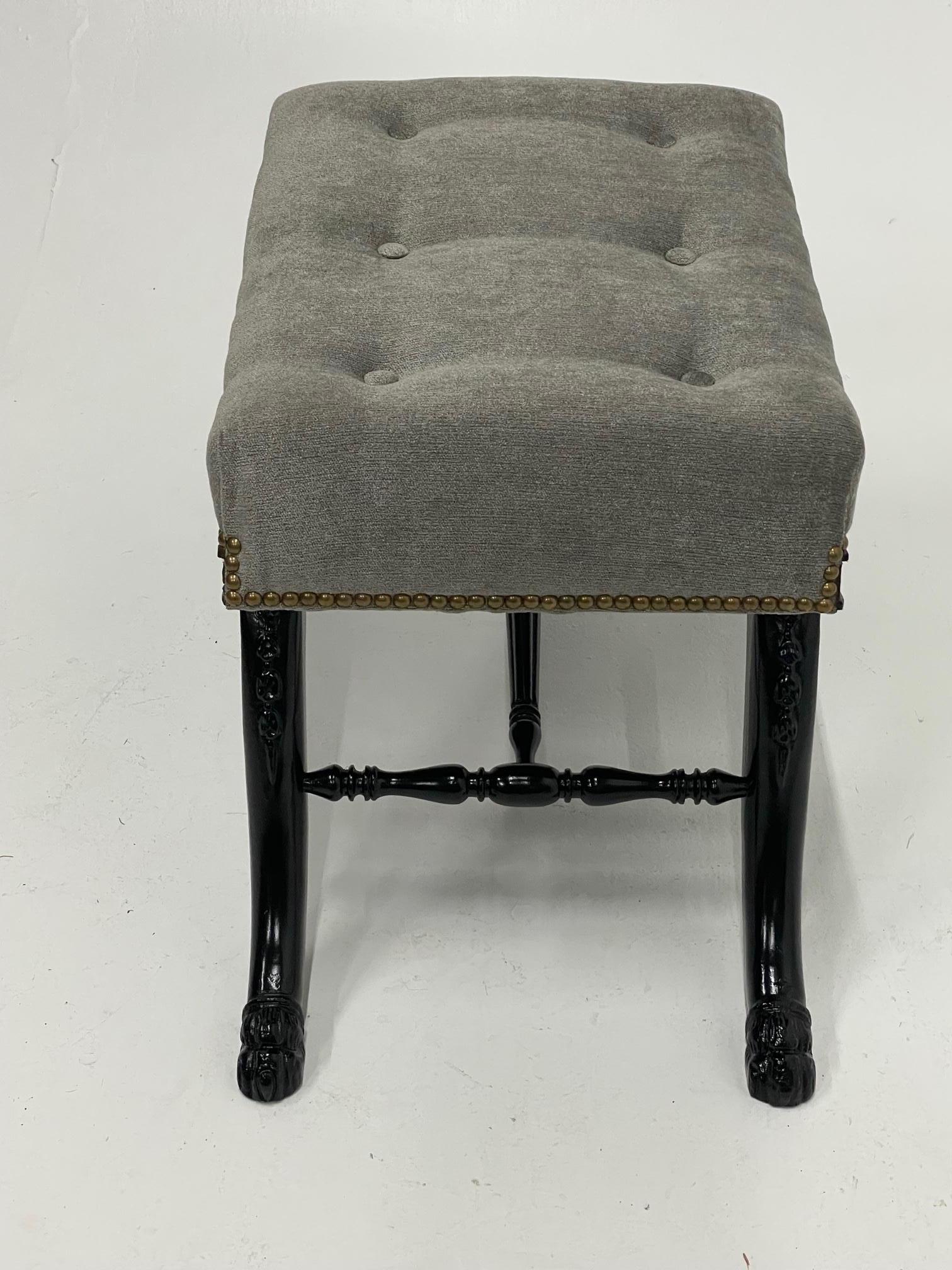 Super handsome Hollywood Regency ebonized carved wood bench having sabre legs that terminate in paw feet and elegant stretcher bars underneath a refined grey flannel tufted seat finished with nailheads.