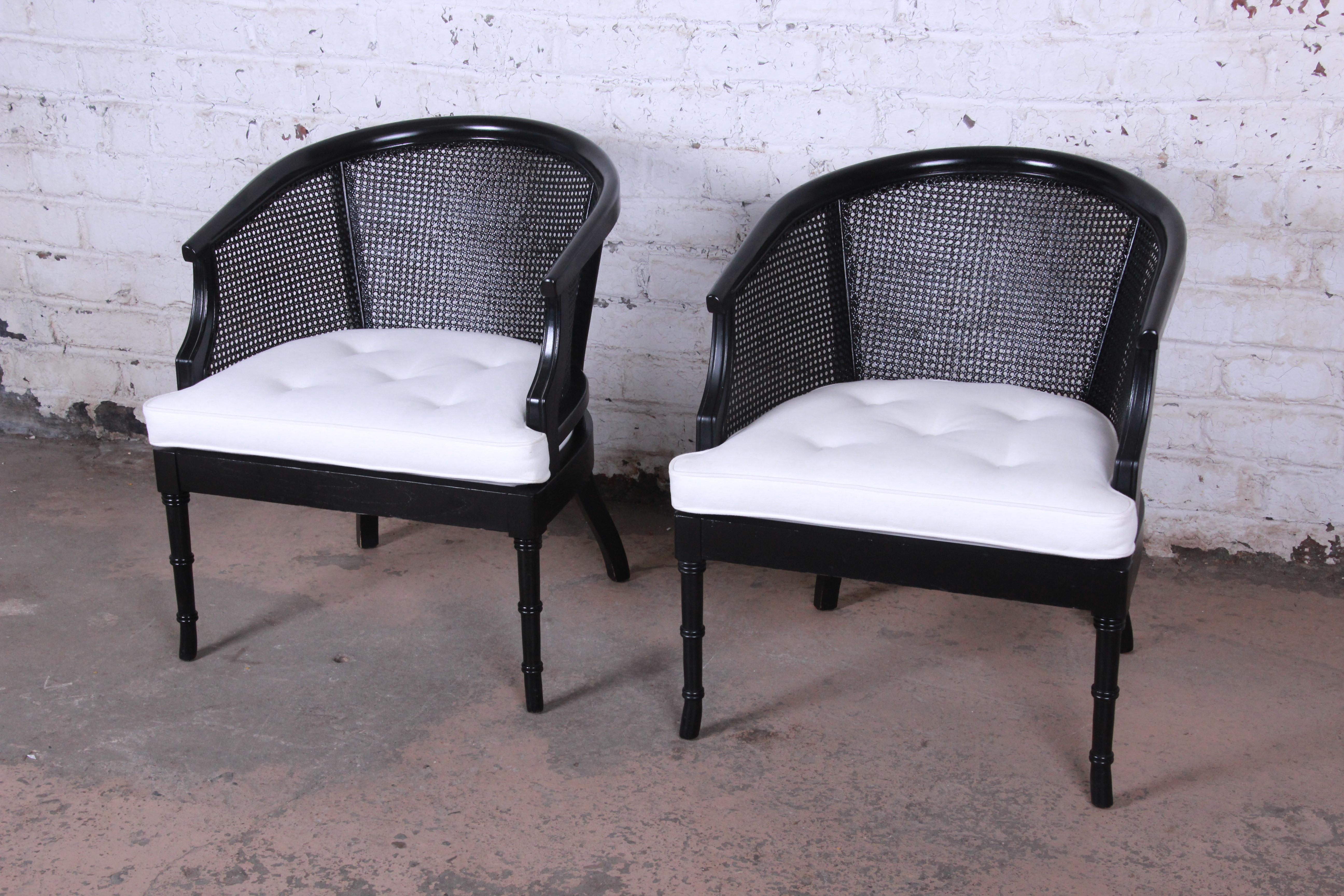 A gorgeous pair of Mid-Century Modern Hollywood Regency faux bamboo and cane barrel back club chairs. The chairs feature stunning ebonized wood frames and tufted white seat cushions. The caning is all intact and seat cushions are in very good