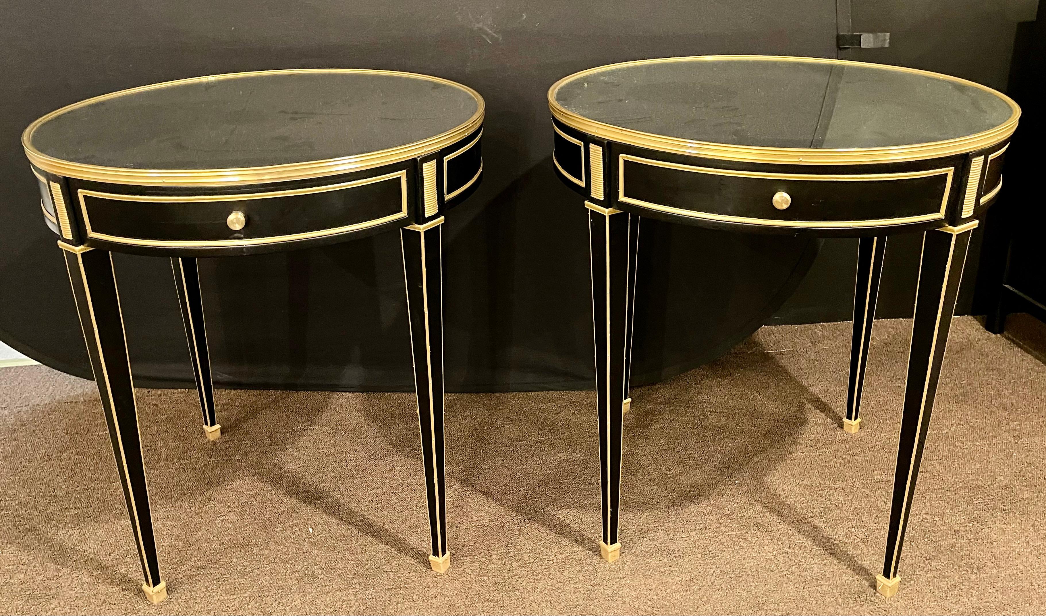 A pair of Jansen style Louis XVI fashioned end or gueridon tables. Each having a bronze framed mirrored top sitting on a single drawer bronzed framed apron with cookie cutter corners. The whole having long sleek tapering legs with bronze framed