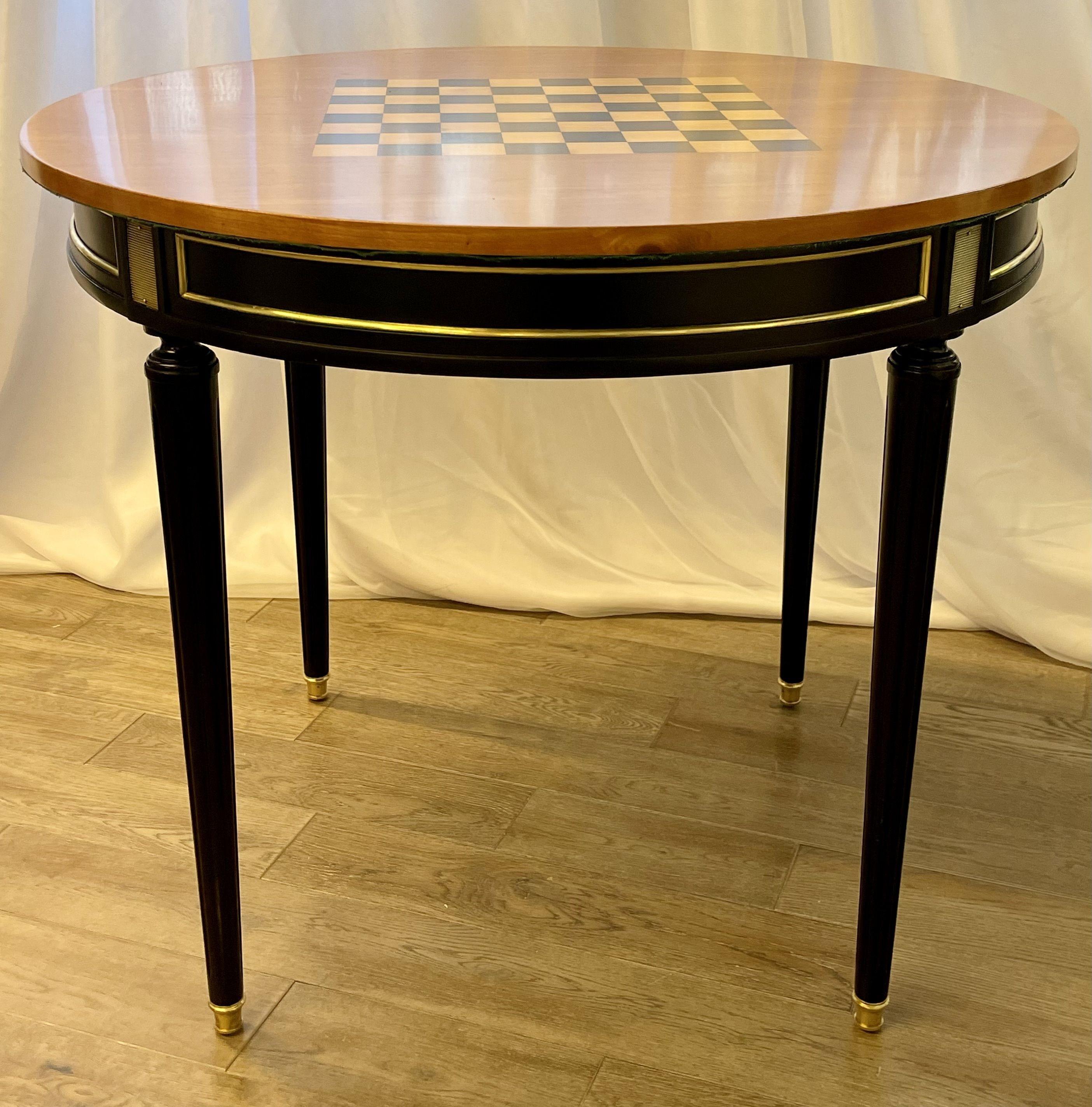 A Hollywood Regency Ebony Game or Card Table having a finely finished checkerboard top on one side and a card table felt on the opposite site. The sleek stylish tapering bronze mounted legs done in a fine ebony finish leading to an open storage