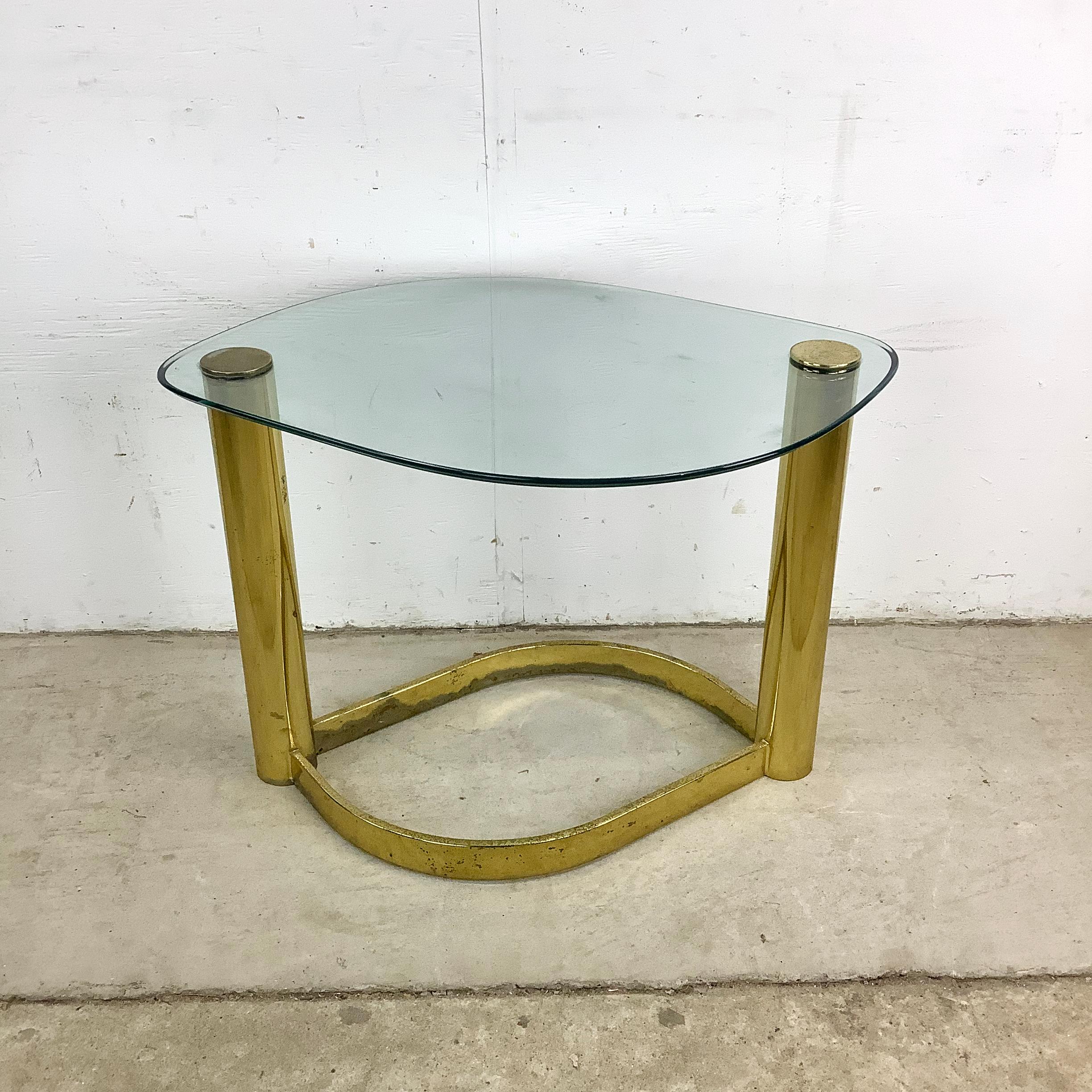 Mélange de luxe et de praticité quotidienne, cette table d'appoint à plateau en verre offre une beauté fonctionnelle avec sa surface en verre en forme de goutte d'eau et sa structure en métal au fini laiton. Inspirée par Leon Rosen pour Pace