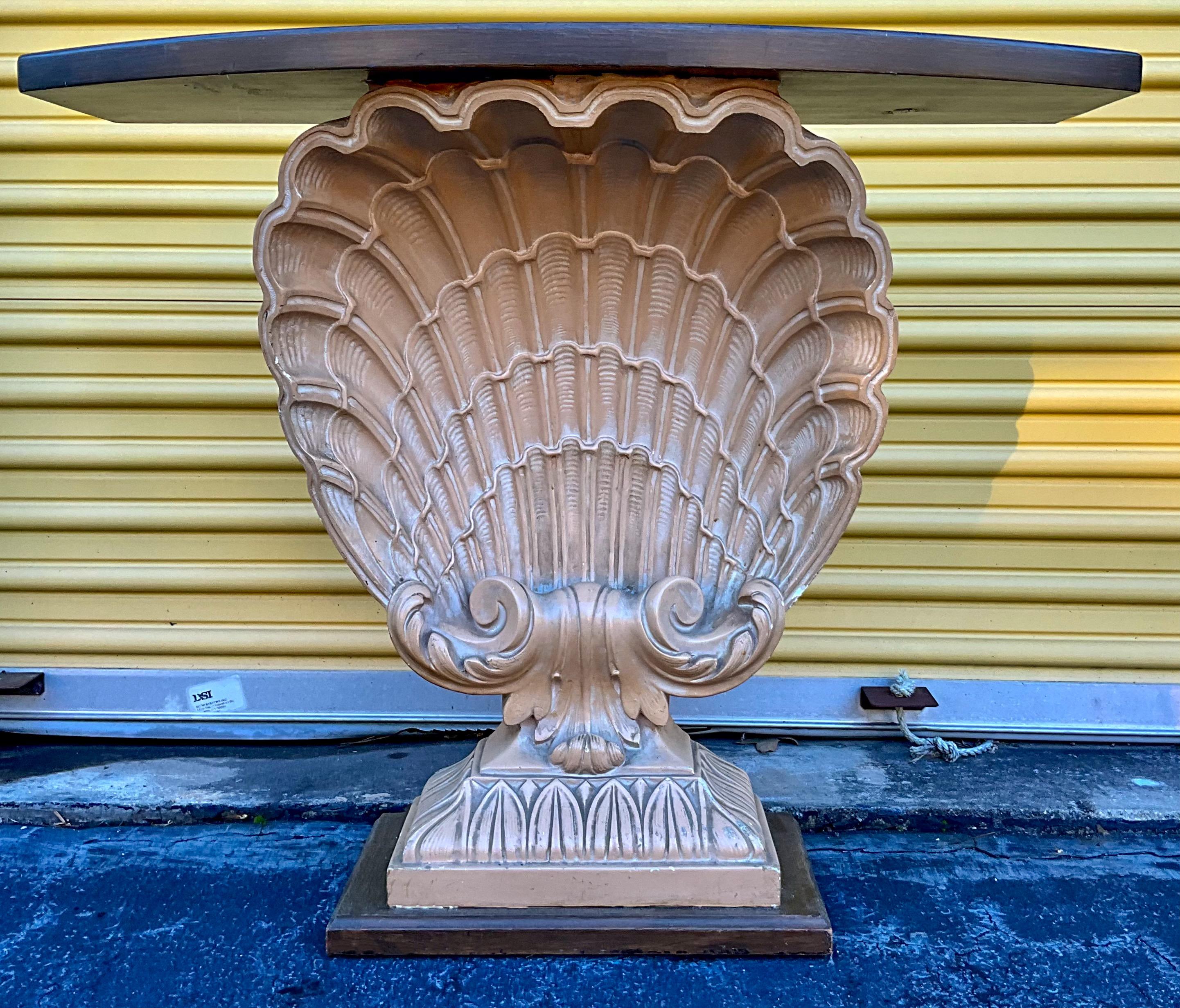 This is a Hollywood Regency Era shell form console table with grotto styling. The shell is cast plaster with a wood top. It is unmarked but an iconic piece for the manufacturer, Grosfeld House. It has lite age wear that doesn’t detract from the