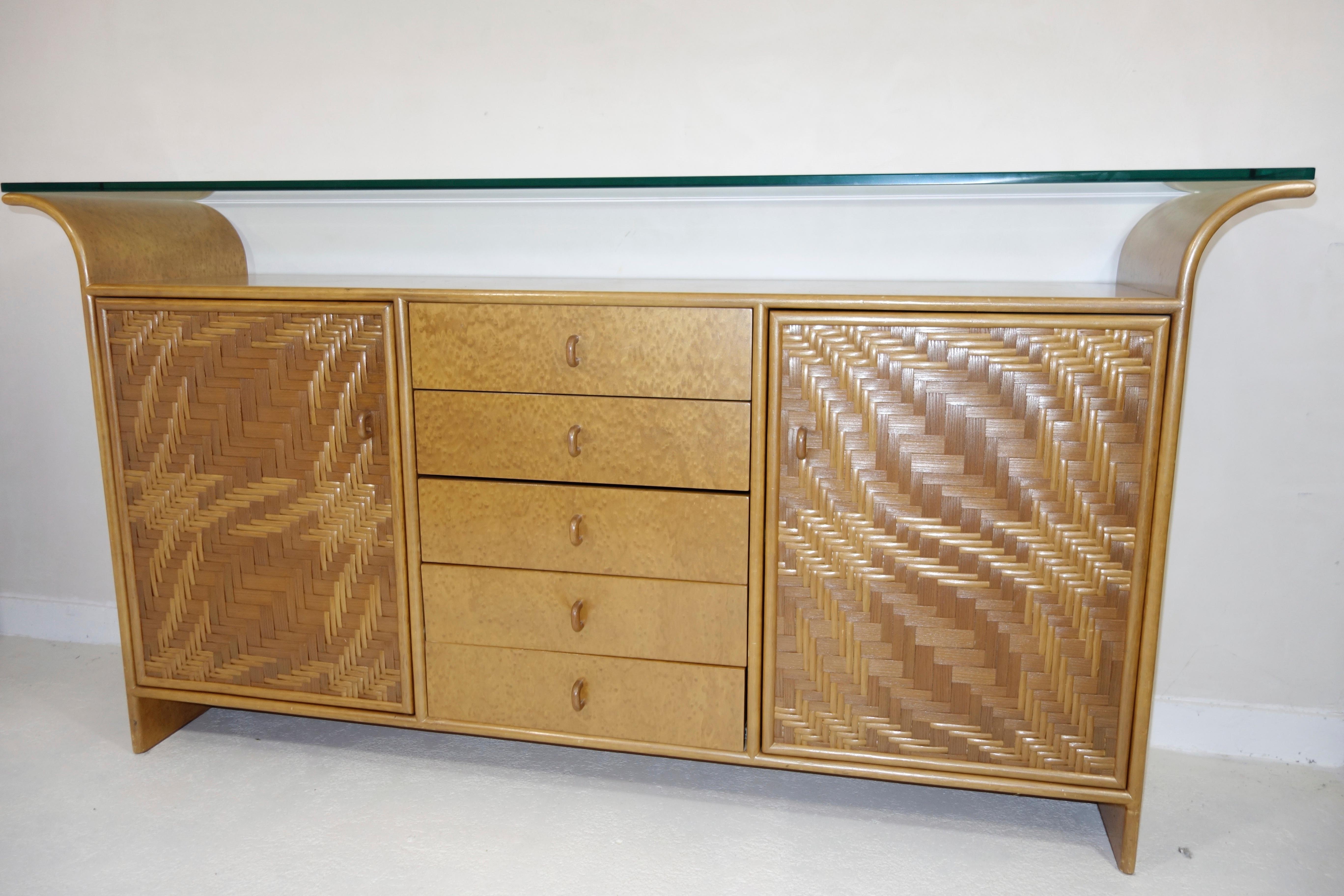 Lovely credenza in Hollywood Regency style made of wood and faux bamboo.
The sideboard has two doors on the sides and five drawers in the middle.
It is elegantly crowned by a thick glass top permitting display space both underneath and on top of