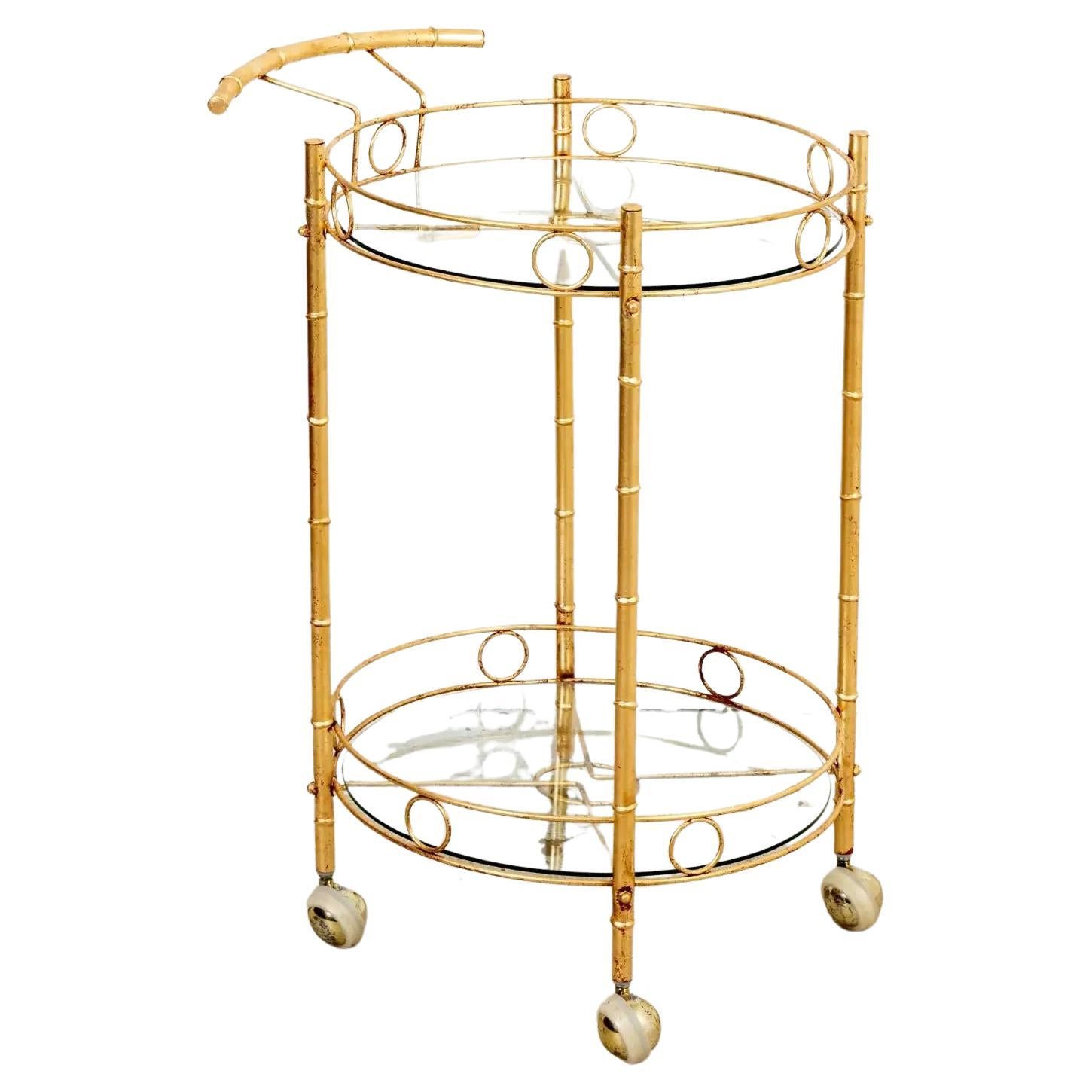 Circa 1960-1970s Hollywood Regency faux bamboo gilt metal round bar cart on ball shaped casters. The drink cart also features two tiers with round glass inserts and disk trim gallery. Made in the United States. Please note of wear consistent with