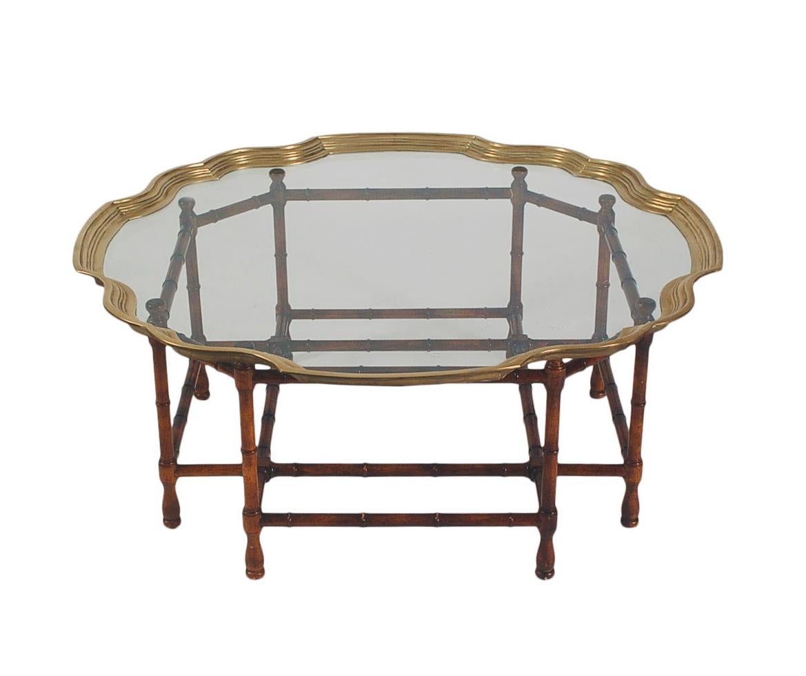 A chic and classic transitional coffee table circa 1960's. It features a faux bamboo wood base with a brass frame and clear glass top.