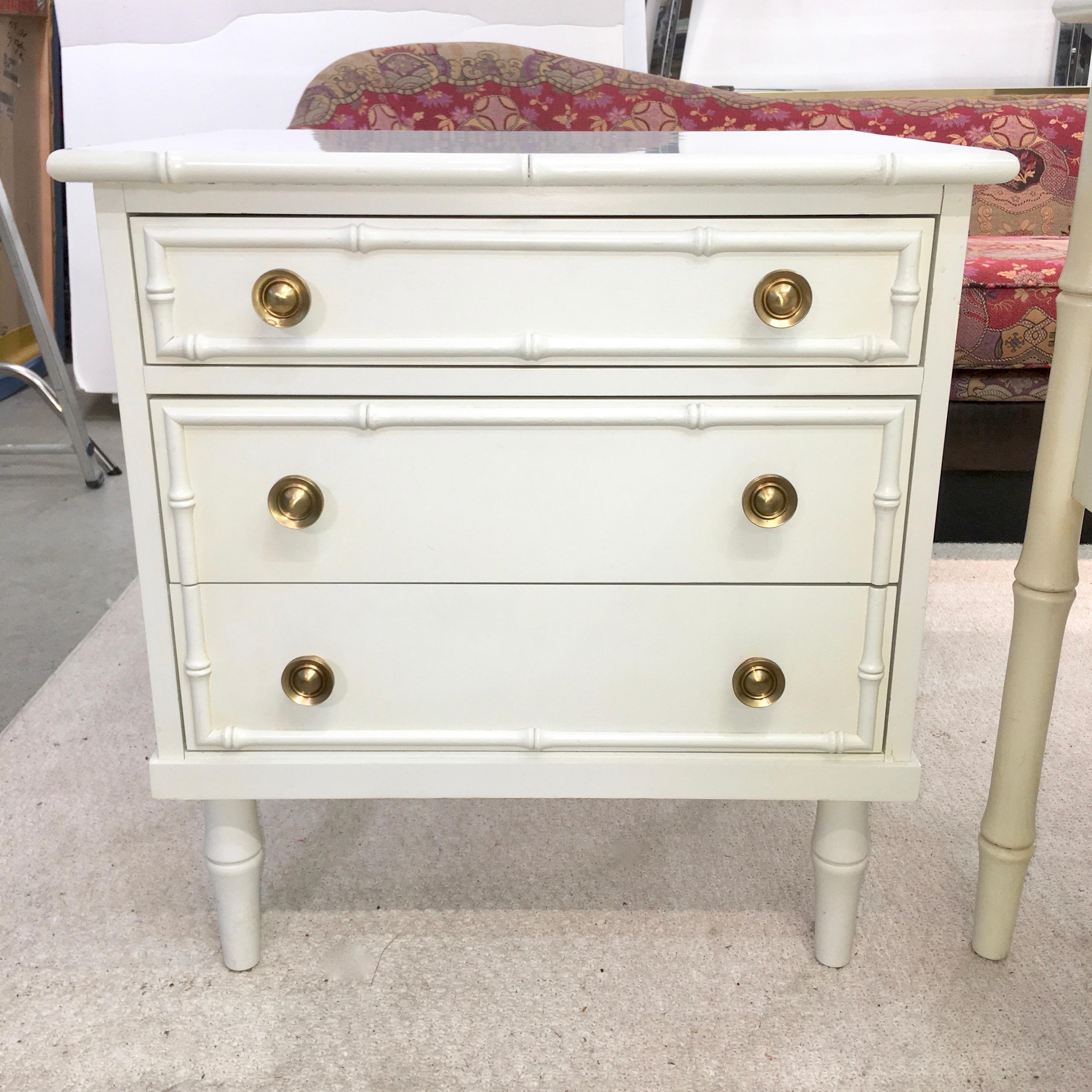 We have two of these upmarket vintage 1960s Hollywood Regency faux bamboo painted wood three drawer small chests or nightstands, attributed to Ficks Reed. One in its original white finish with white laminate top and posh solid brass hardware. The