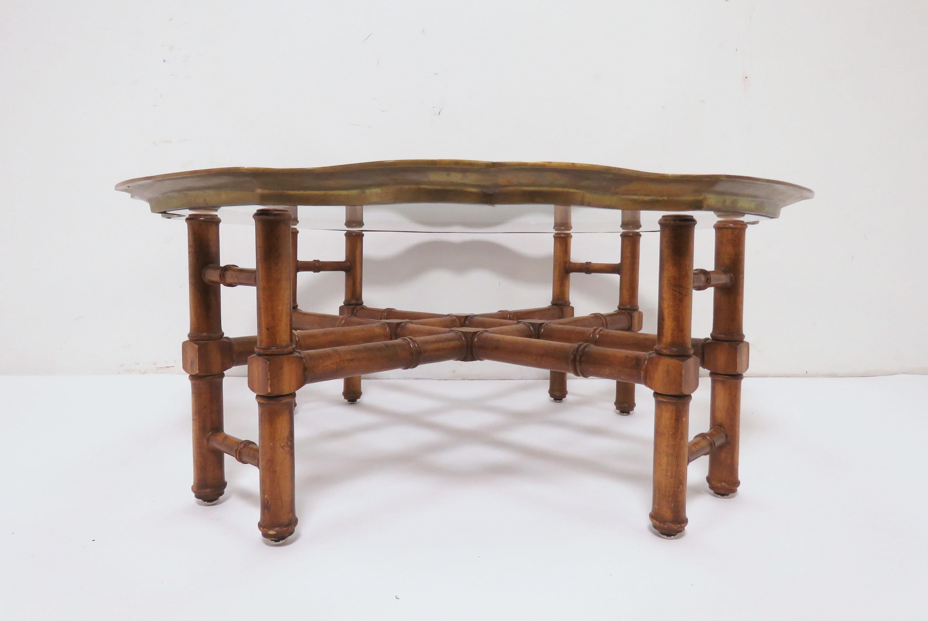 Coffee table in an elegant far East style, faux bamboo trestle form base and a solid brass pie-crust framed glass top. These tables are usually attributed to Baker Furniture Co.