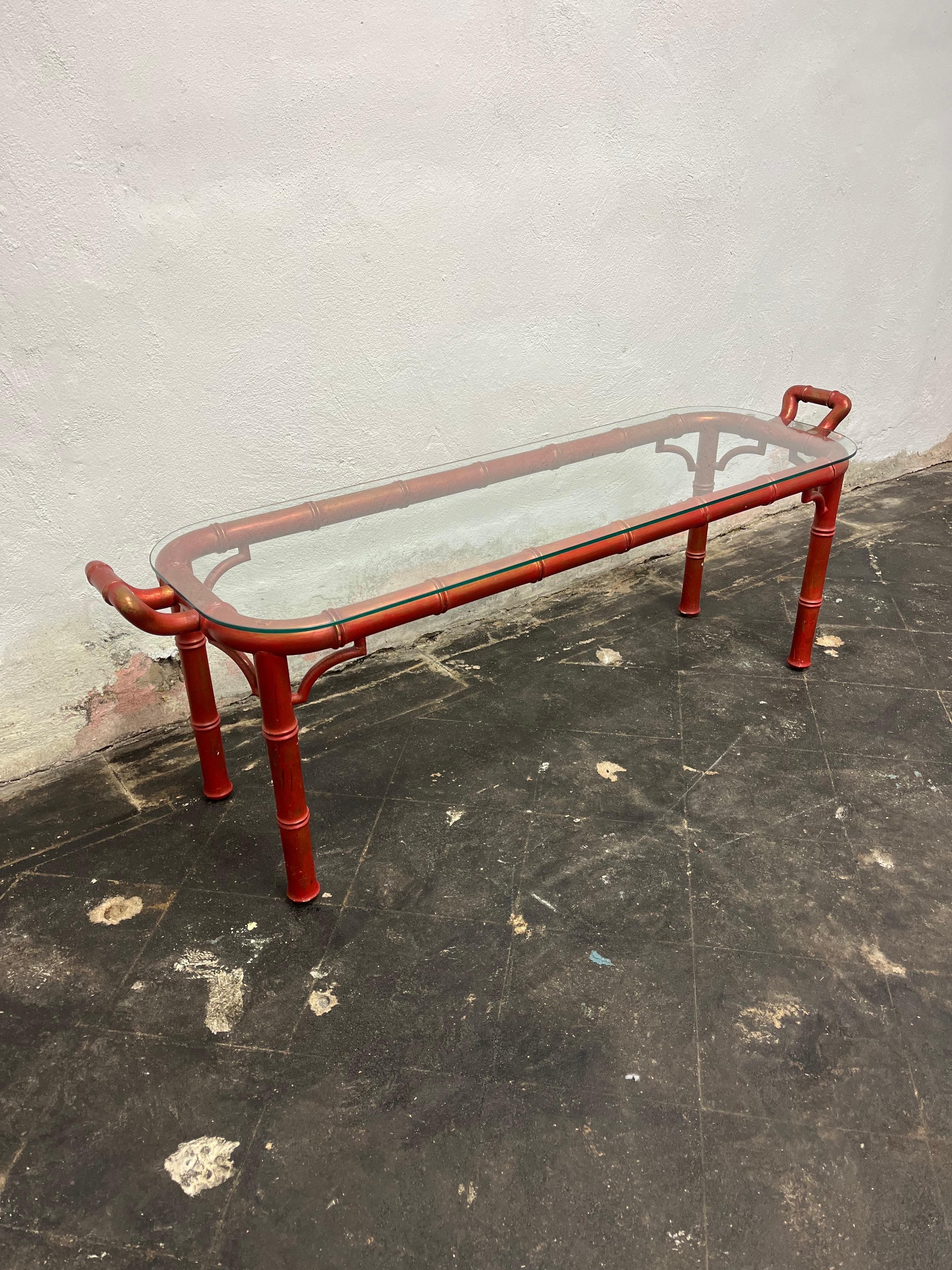 Mid-Century Modern Palm Regency style glass and wood handled cocktail table featuring a painted finish in crimson over gold. Bamboo style frame with rounded edge glass top. Could also be topped converted into a bench. In the style of Dorothy Draper