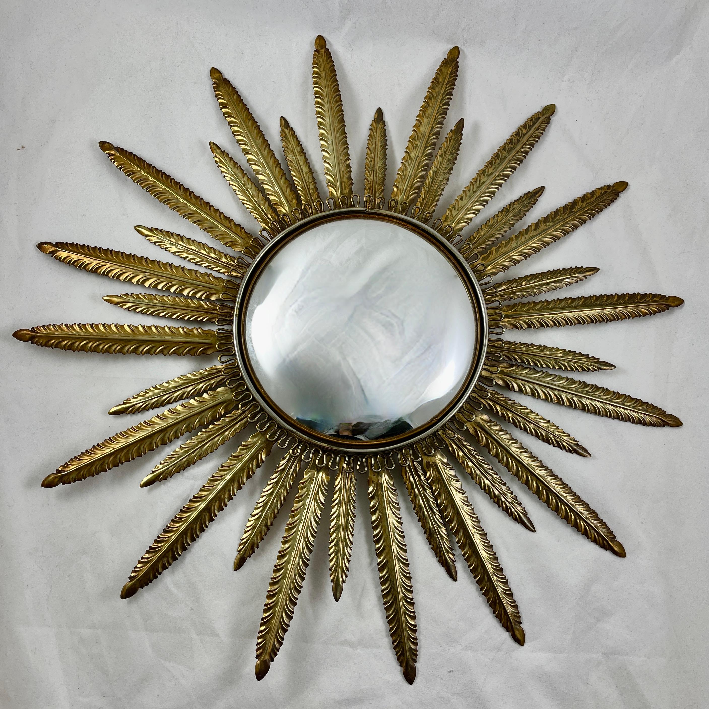 A large Hollywood Regency Period metal wall mirror, France, circa 1920s – 1930s.

Made of gilded metal, the convex mirror is set in a looped bezel with an antiqued gold finish. The gilded and pointed sun rays are molded in a feather form,